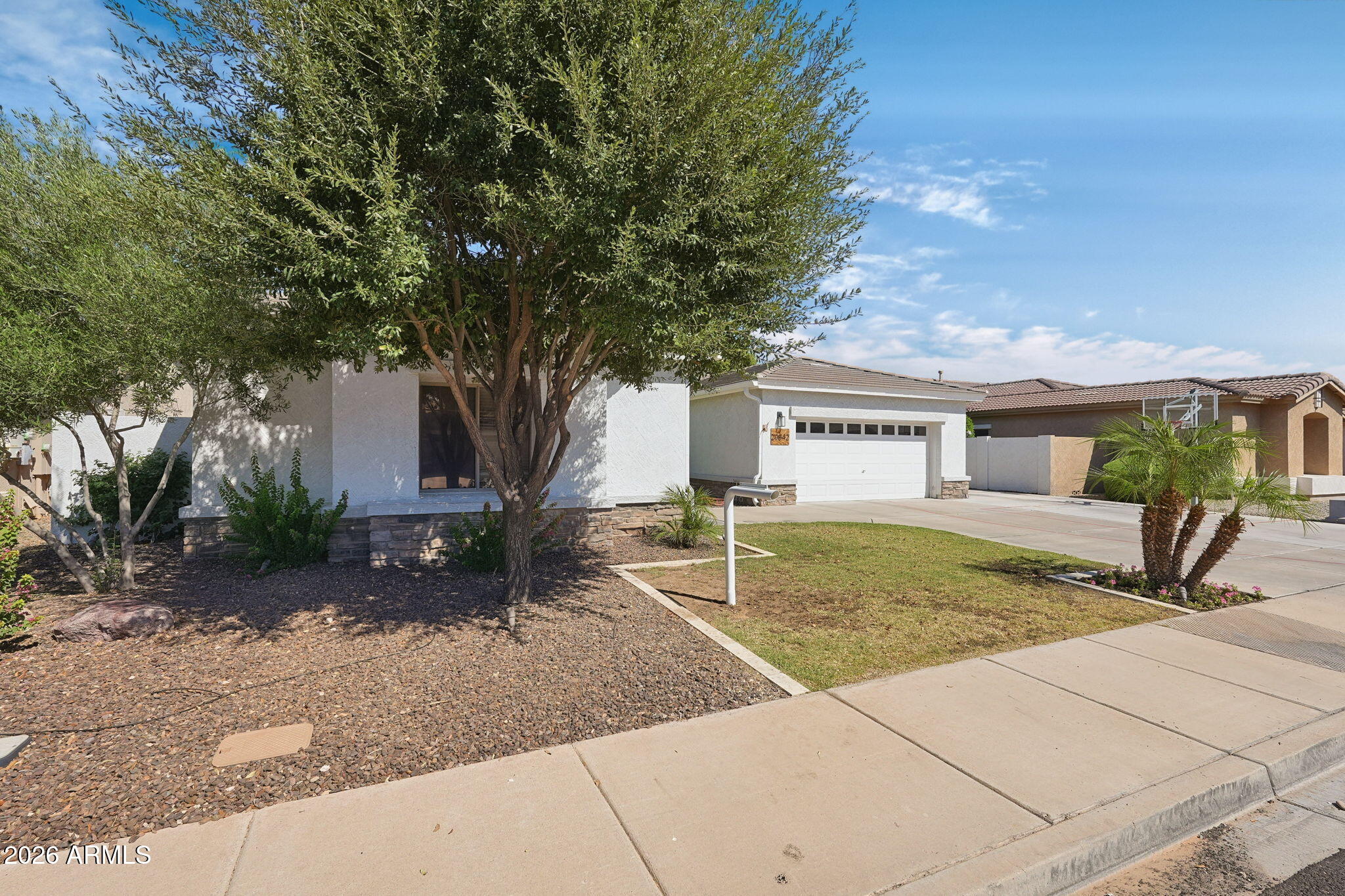 Single-story home's front exterior with a large shade tree, stone base, and two-car garage.
