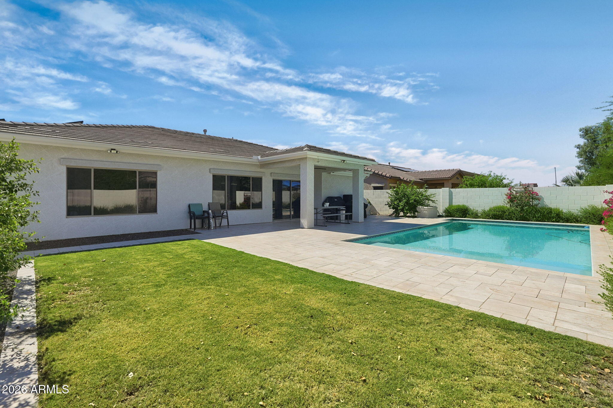 Home’s rear patio and swimming pool beside a paved deck and green lawn.