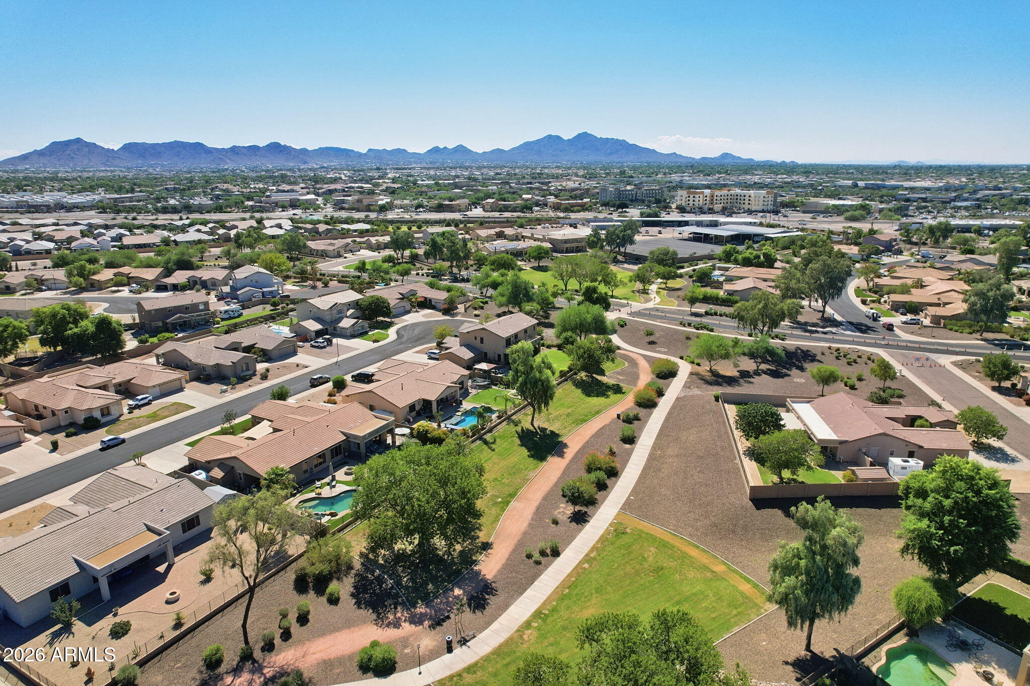 Aerial view of a suburban neighborhood with landscaped park paths and mountains in the distance.