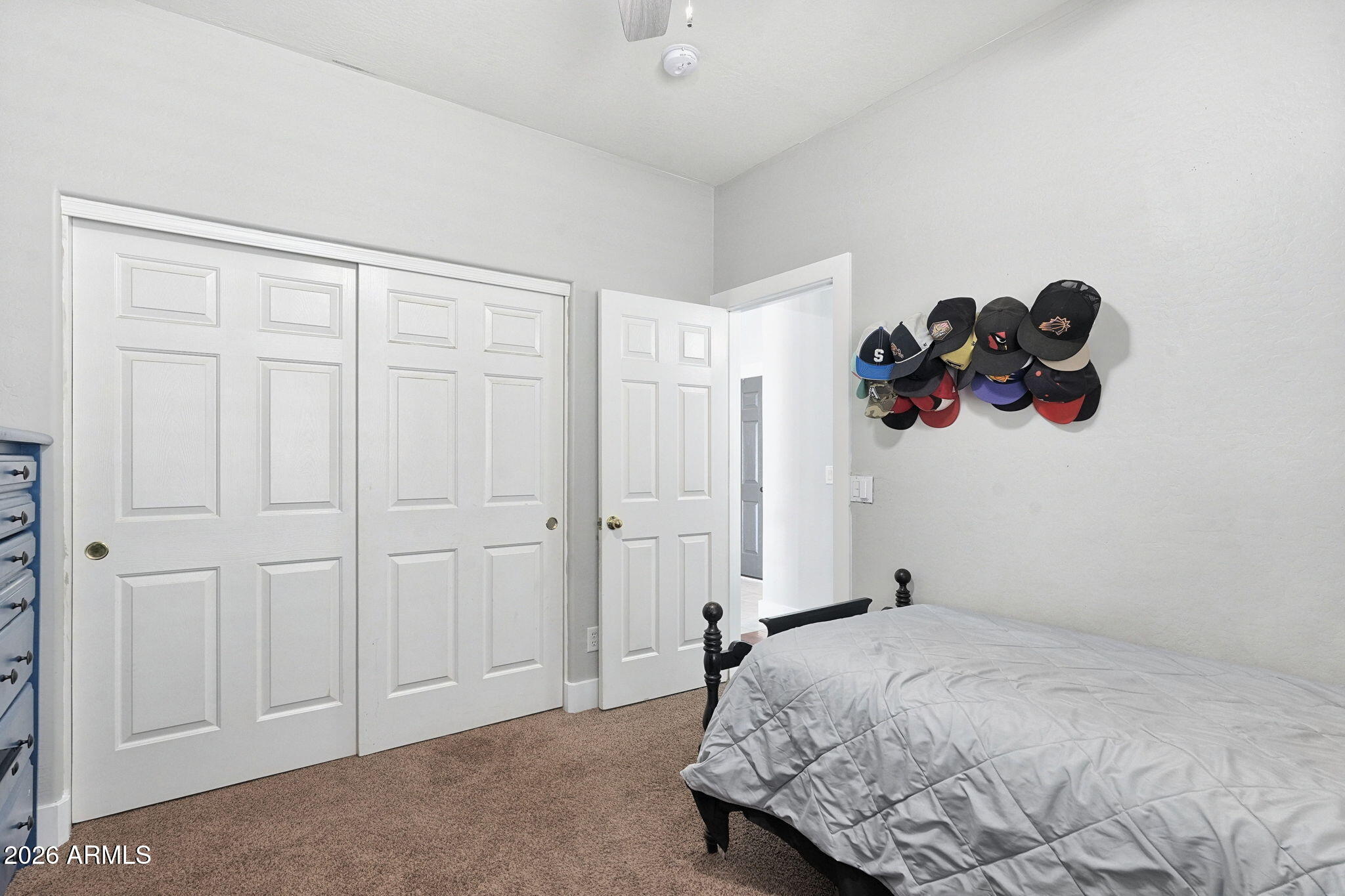 Bedroom with white paneled closet doors, a gray quilted bed, and baseball caps displayed on the wall.