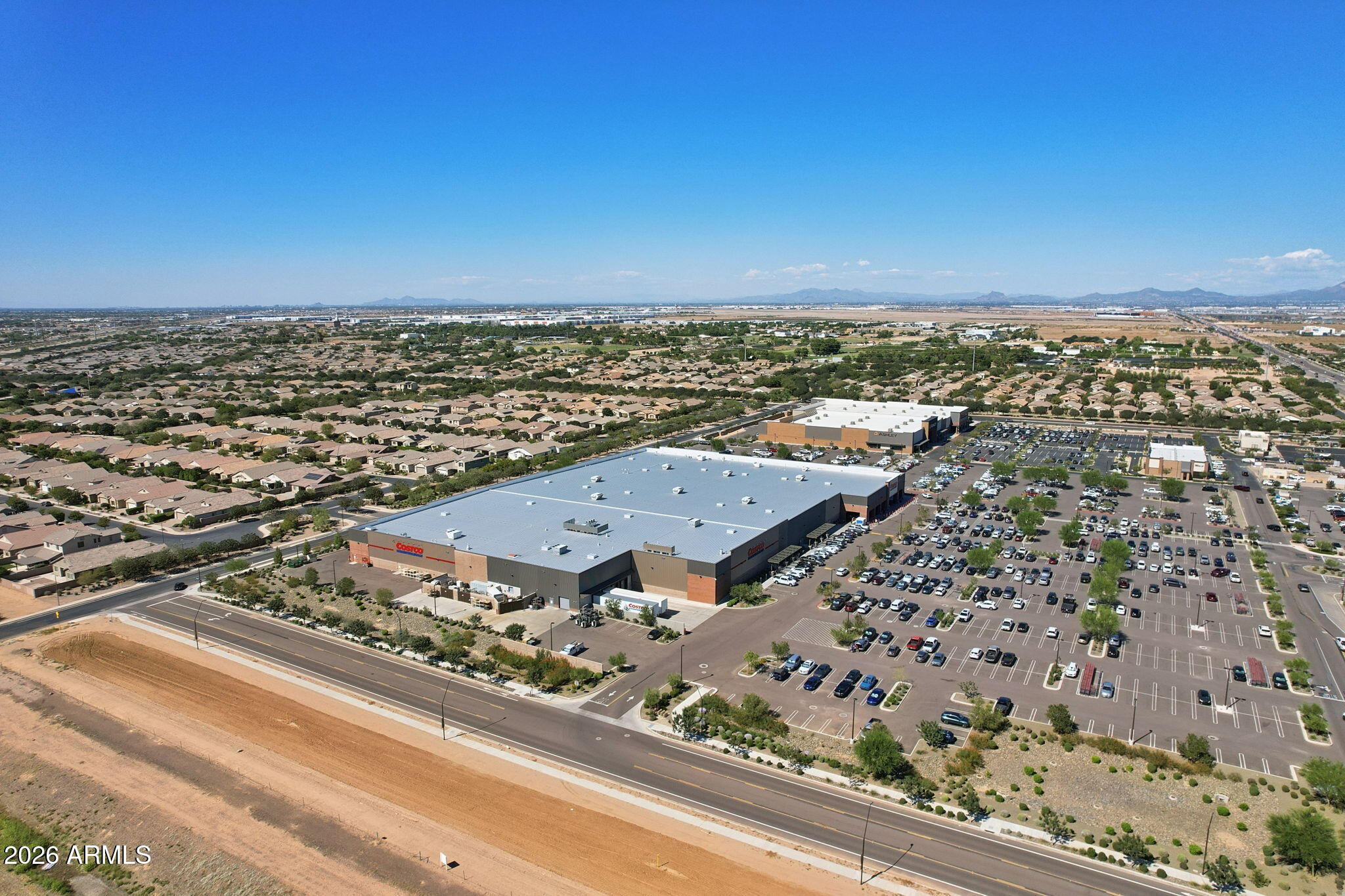 Aerial view of a Costco warehouse and parking lot beside suburban neighborhoods, with distant mountains.
