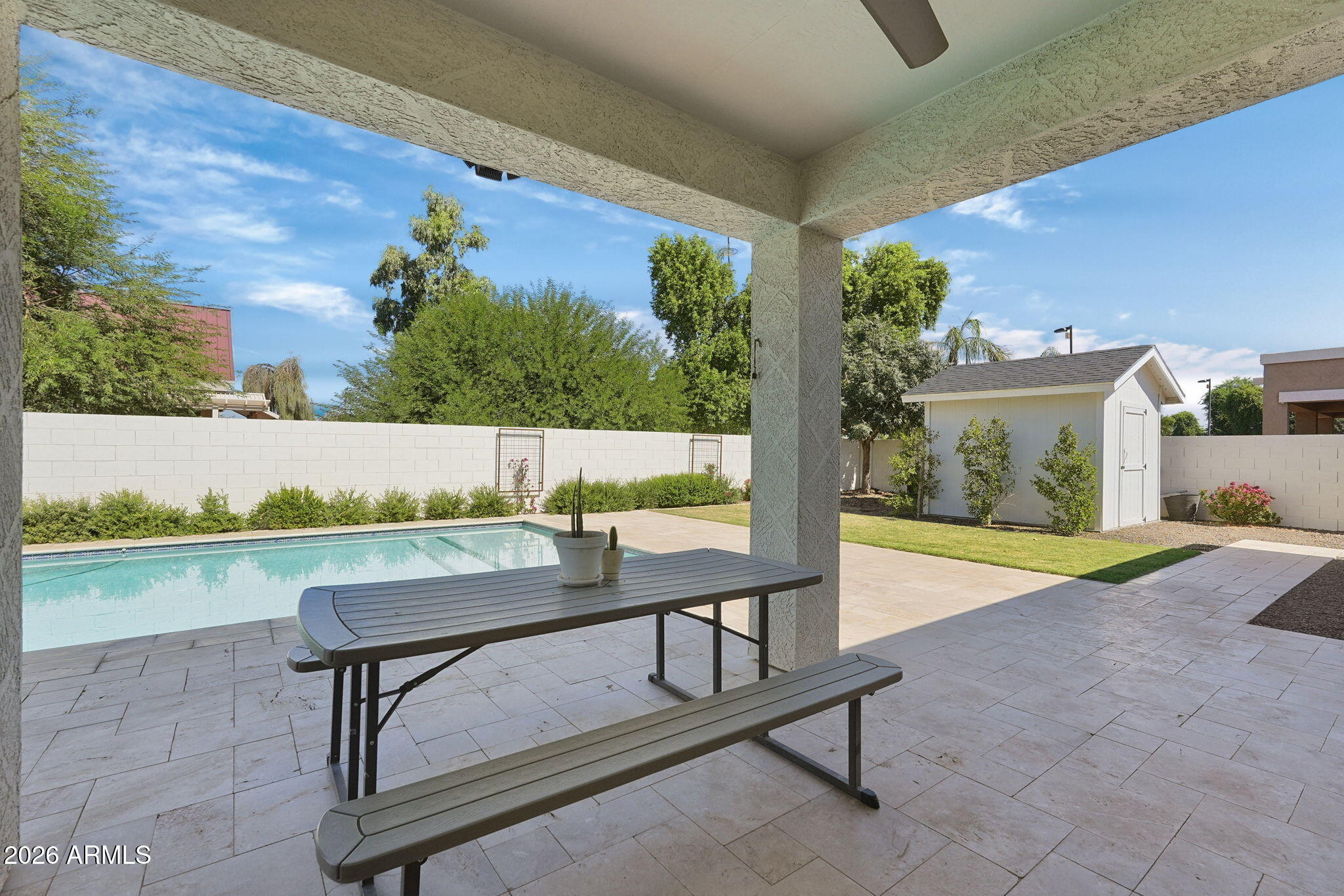 Covered patio with a picnic table overlooks a backyard pool, lawn, and storage shed.
