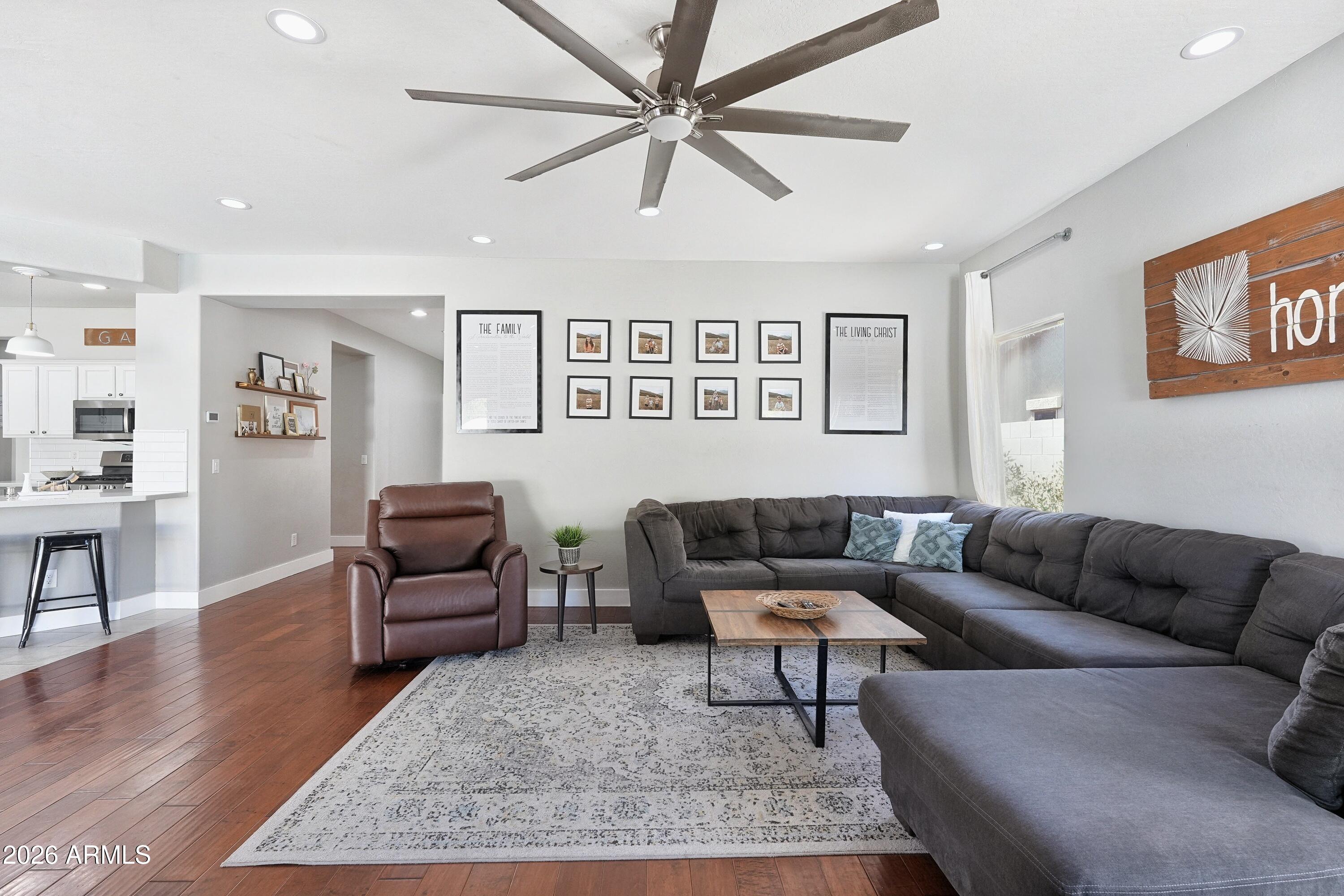 Living room with a large gray sectional, brown leather recliner, patterned rug, and open kitchen.