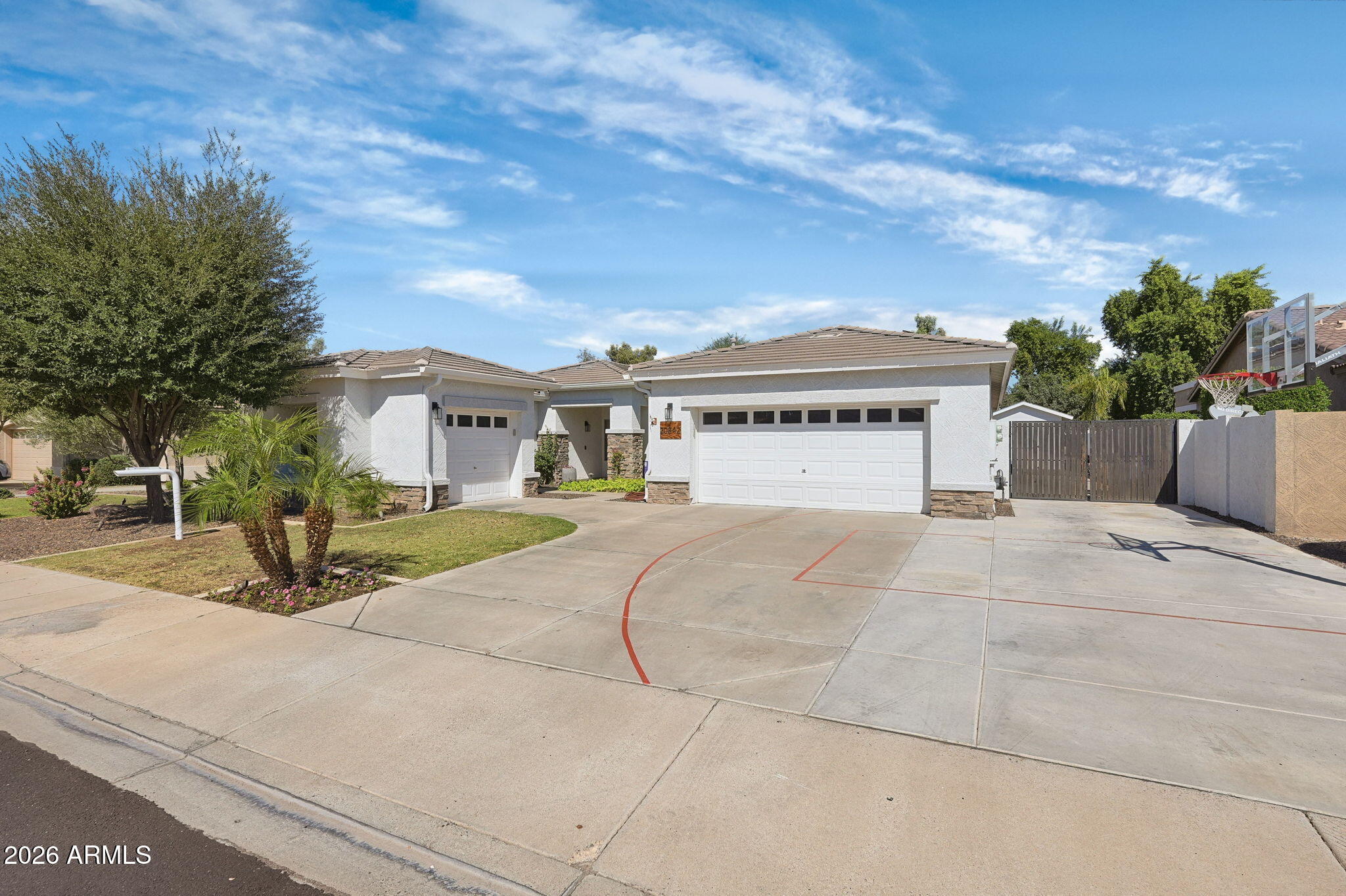 Single-story stucco home with two garages, palm landscaping, and a driveway basketball court.