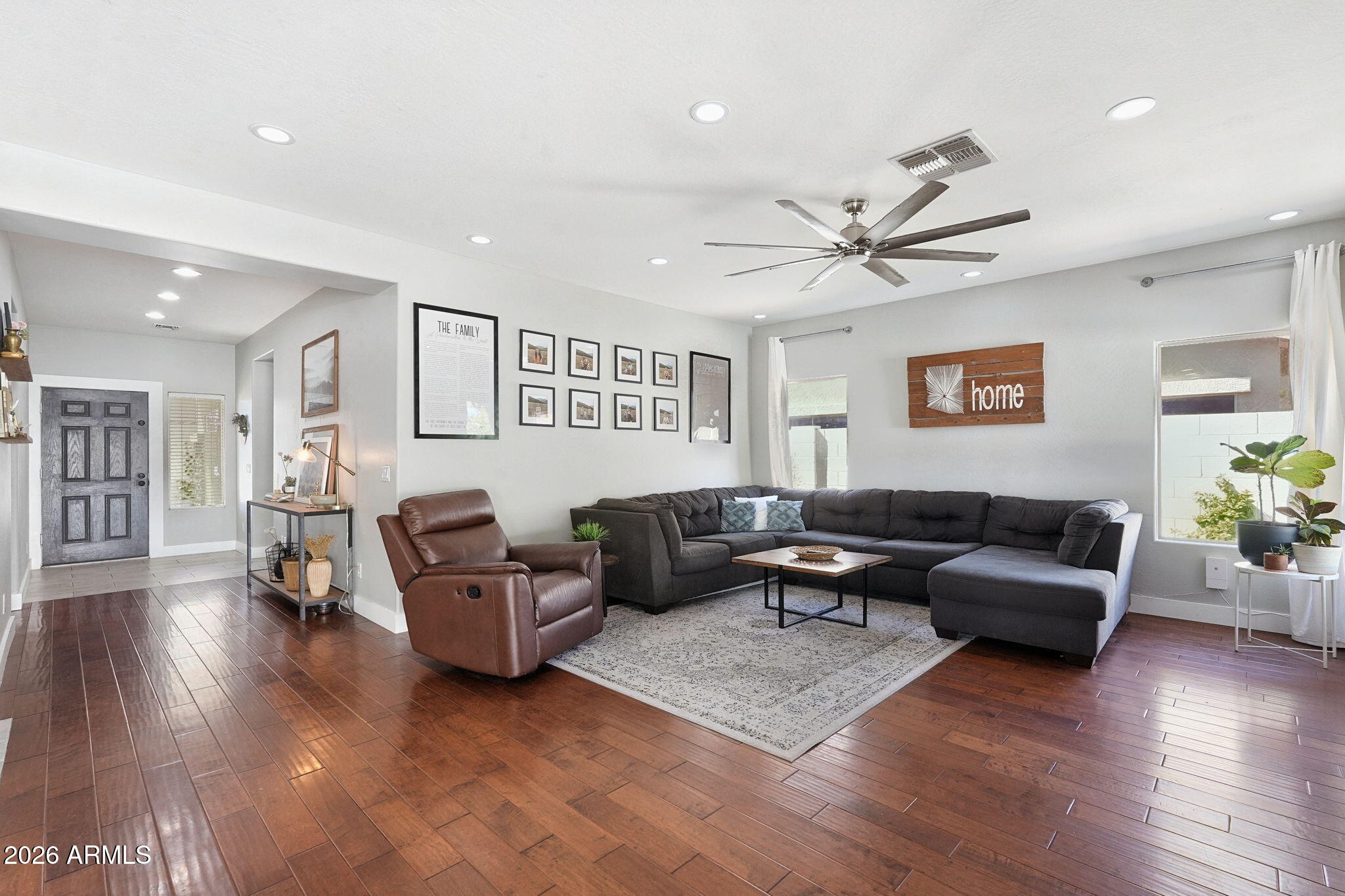 Living room with a dark gray sectional, brown leather recliner, and wood-look tile flooring.