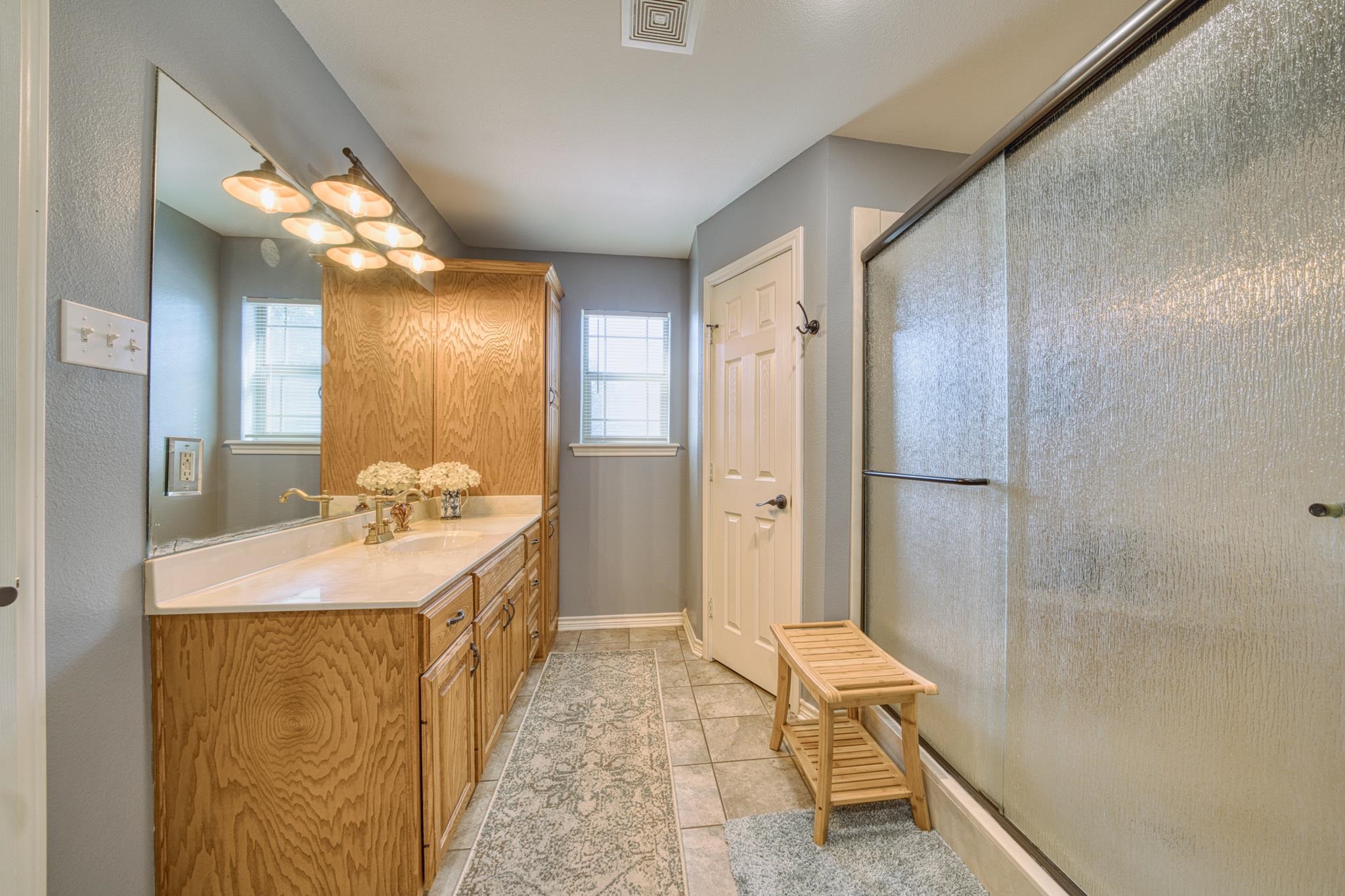 Bathroom with a long oak vanity, large mirror, and glass shower with a wooden bench.