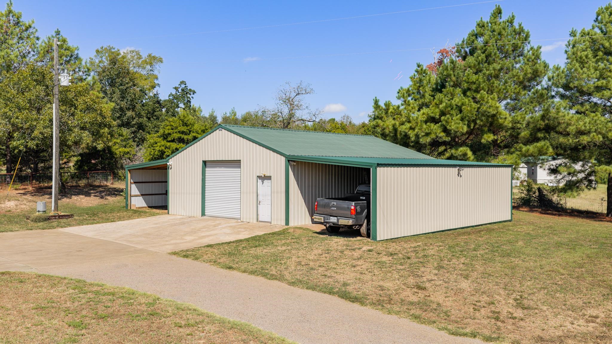 Metal outbuilding with green roof, multiple garage bays, and a pickup truck on a grassy lot.