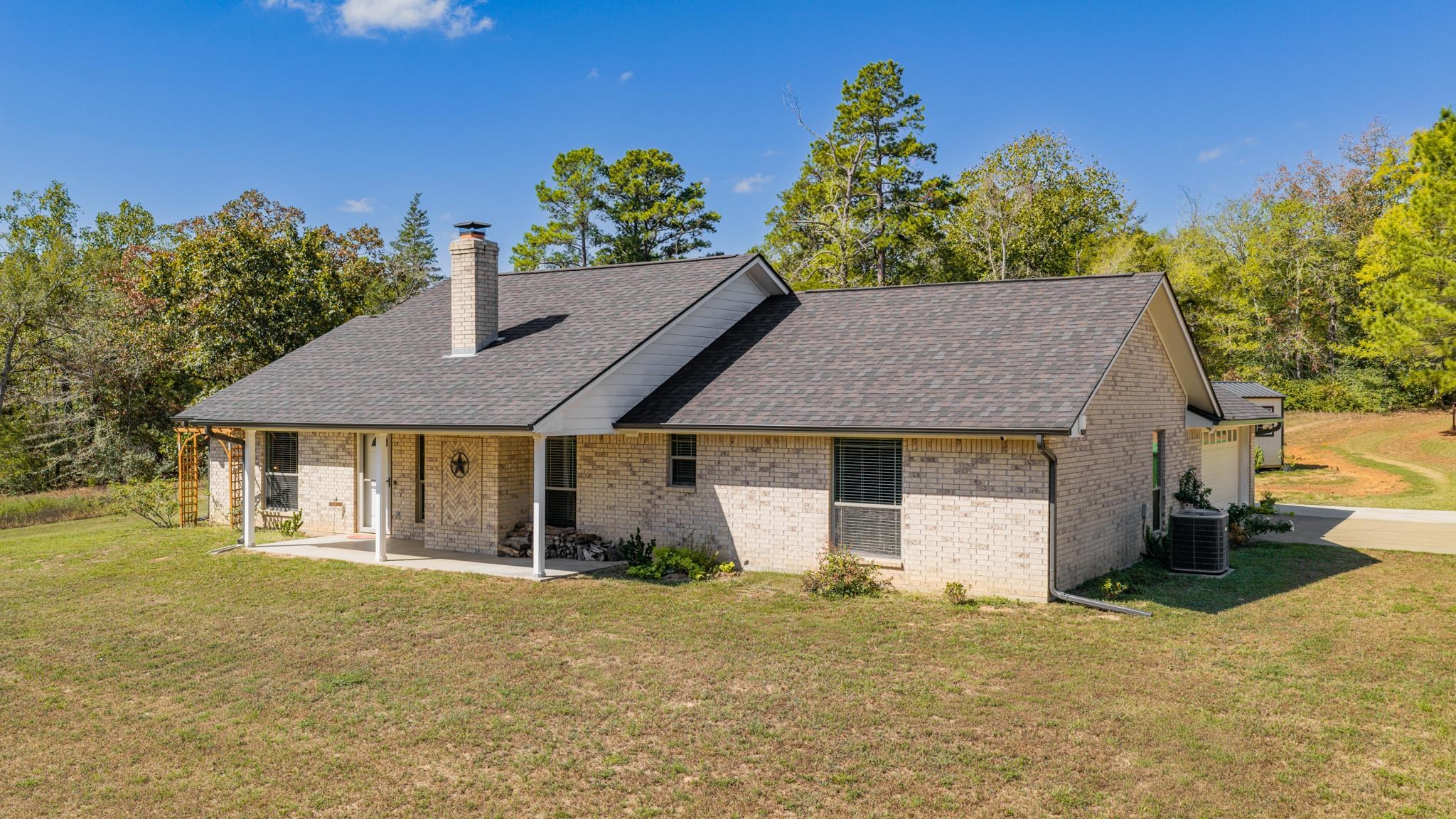 Light brick ranch home with a covered porch, chimney, and attached garage on a grassy lot.