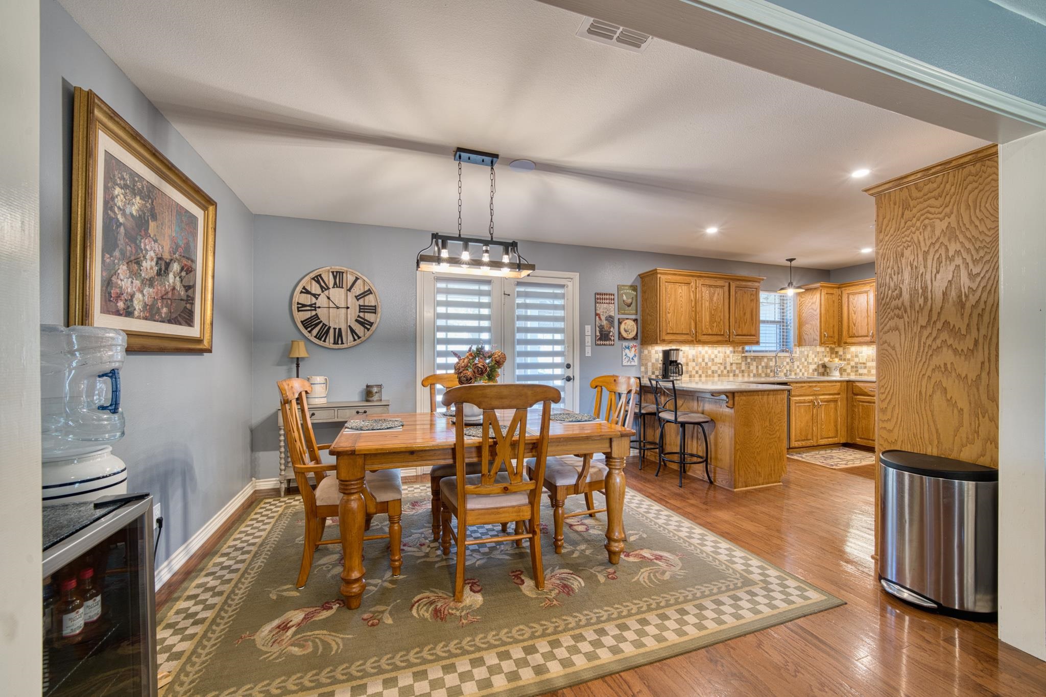 Dining room with a wooden table and chairs, patterned rug, and adjoining oak-cabinet kitchen.