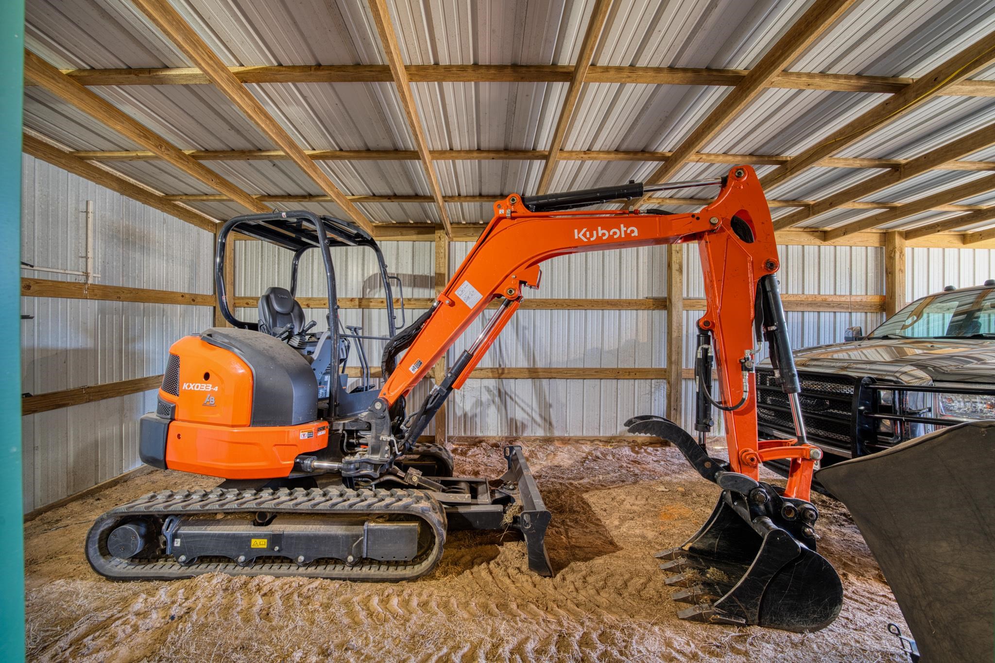 Equipment shed with an orange Kubota excavator parked beside a black pickup truck.