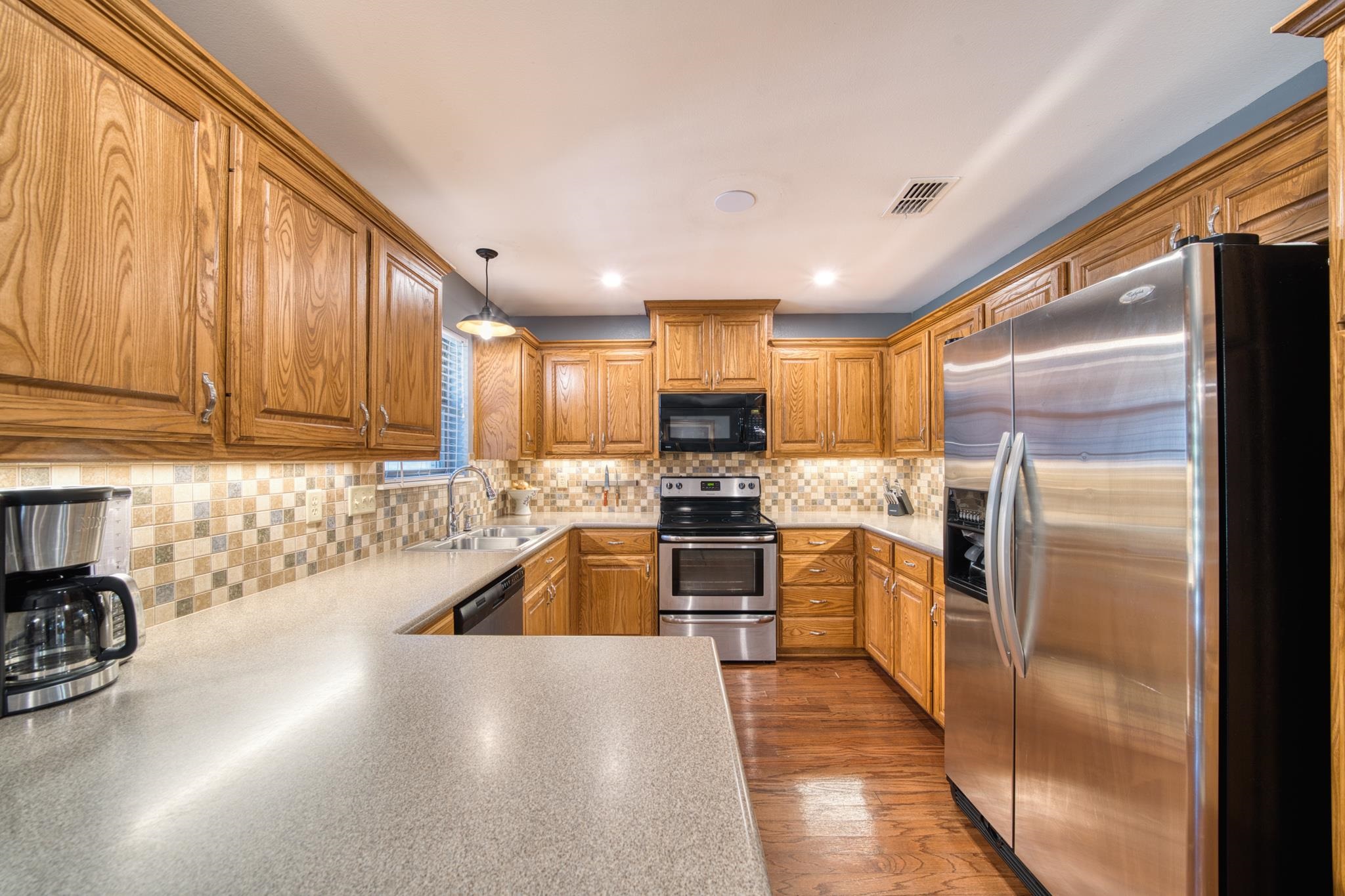Kitchen with honey-toned wood cabinets, tiled backsplash, and stainless steel appliances.