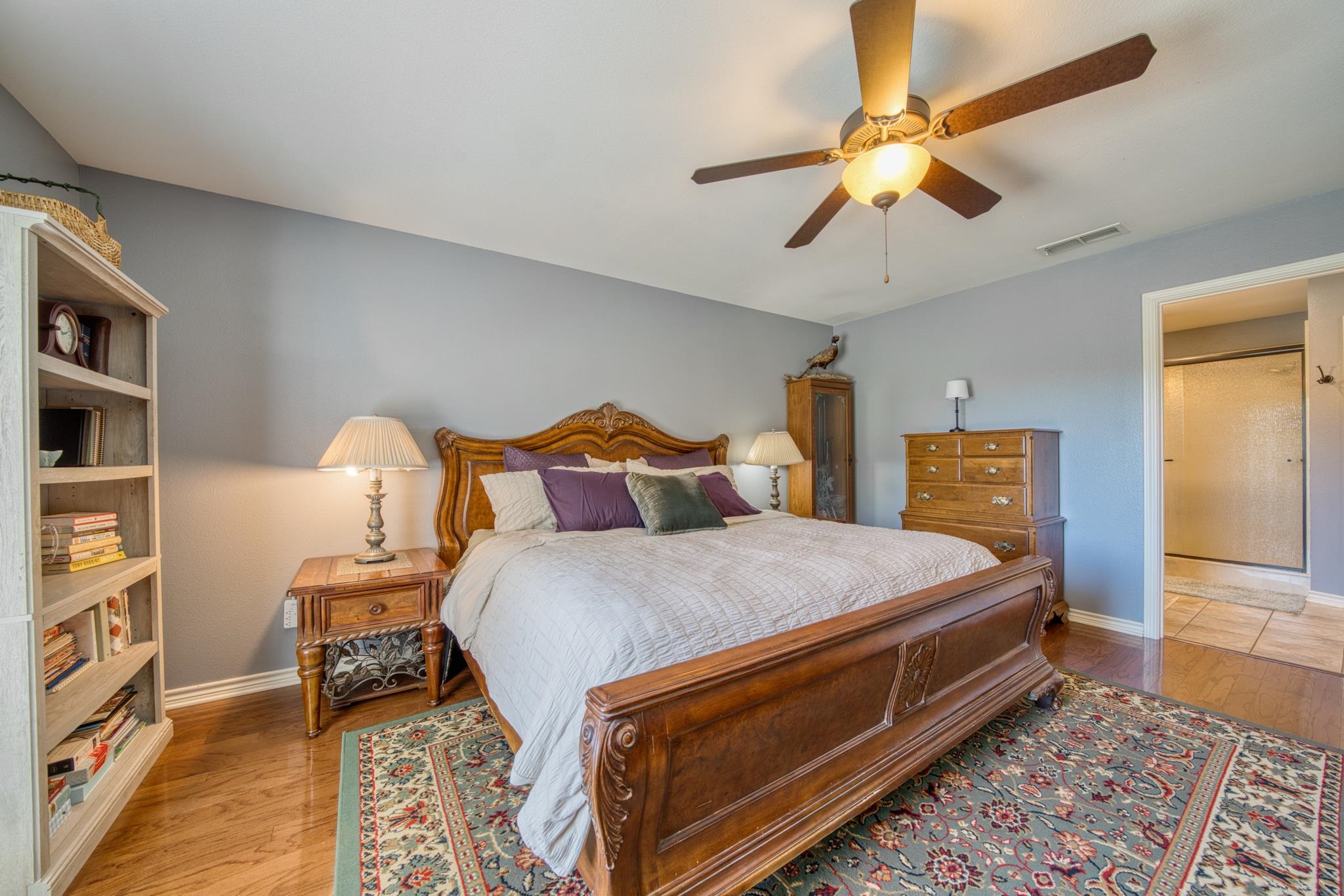 Bedroom with a carved wooden bed, ceiling fan, built-in bookshelf, and patterned rug.