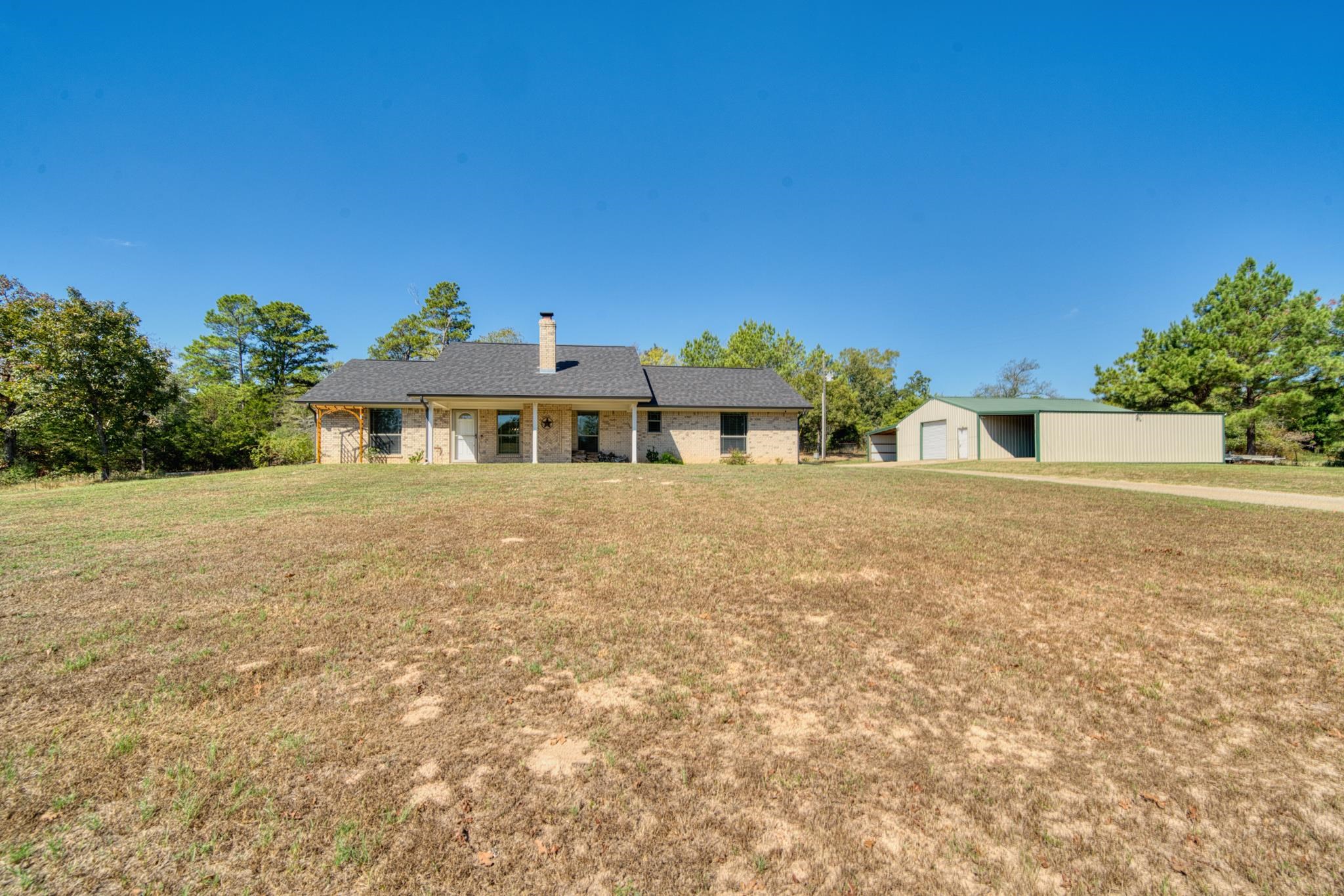 Brick house and large metal outbuilding beyond a broad dry lawn.