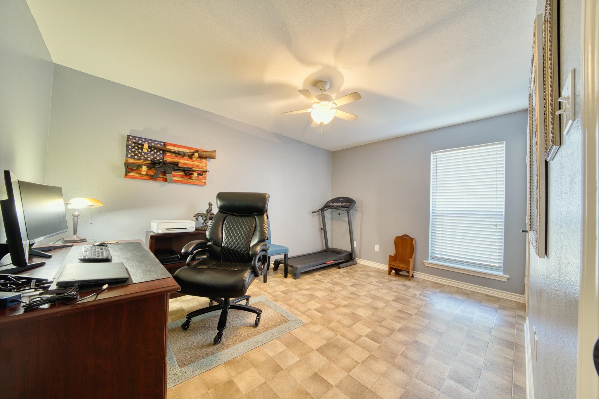 Home office with a wooden desk, black chair, treadmill, and American flag display.