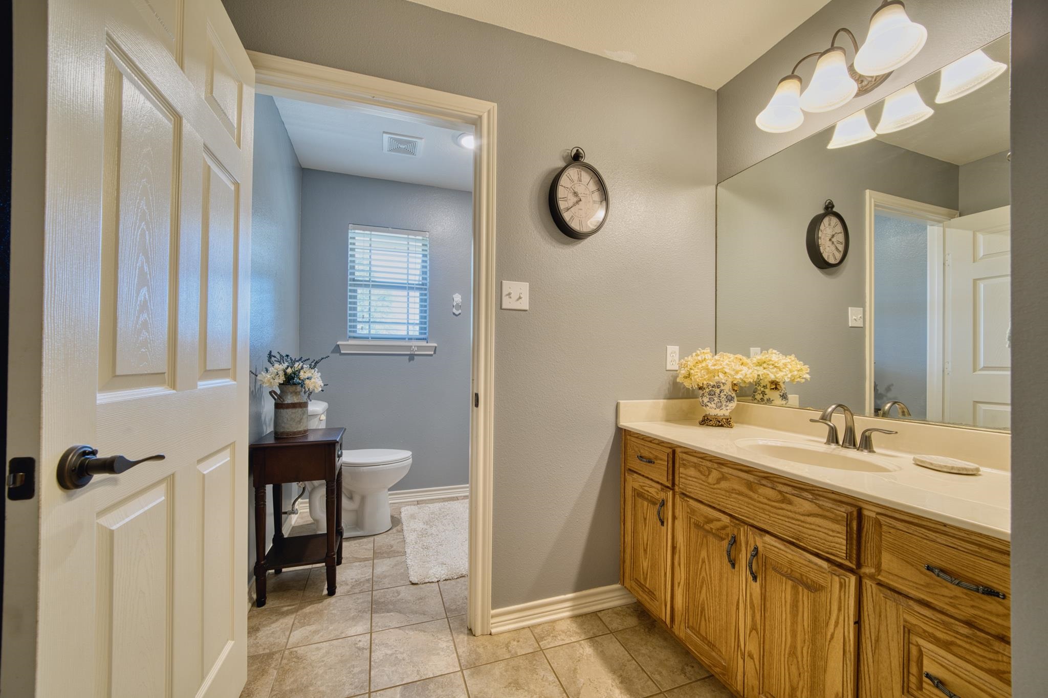 Bathroom with a long oak vanity and mirror beside a separate toilet room with a window.