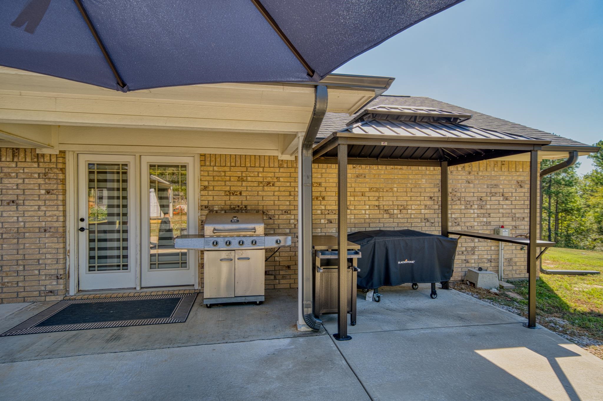Covered brick patio with a stainless-steel grill and covered griddle beneath a metal-roofed shelter.