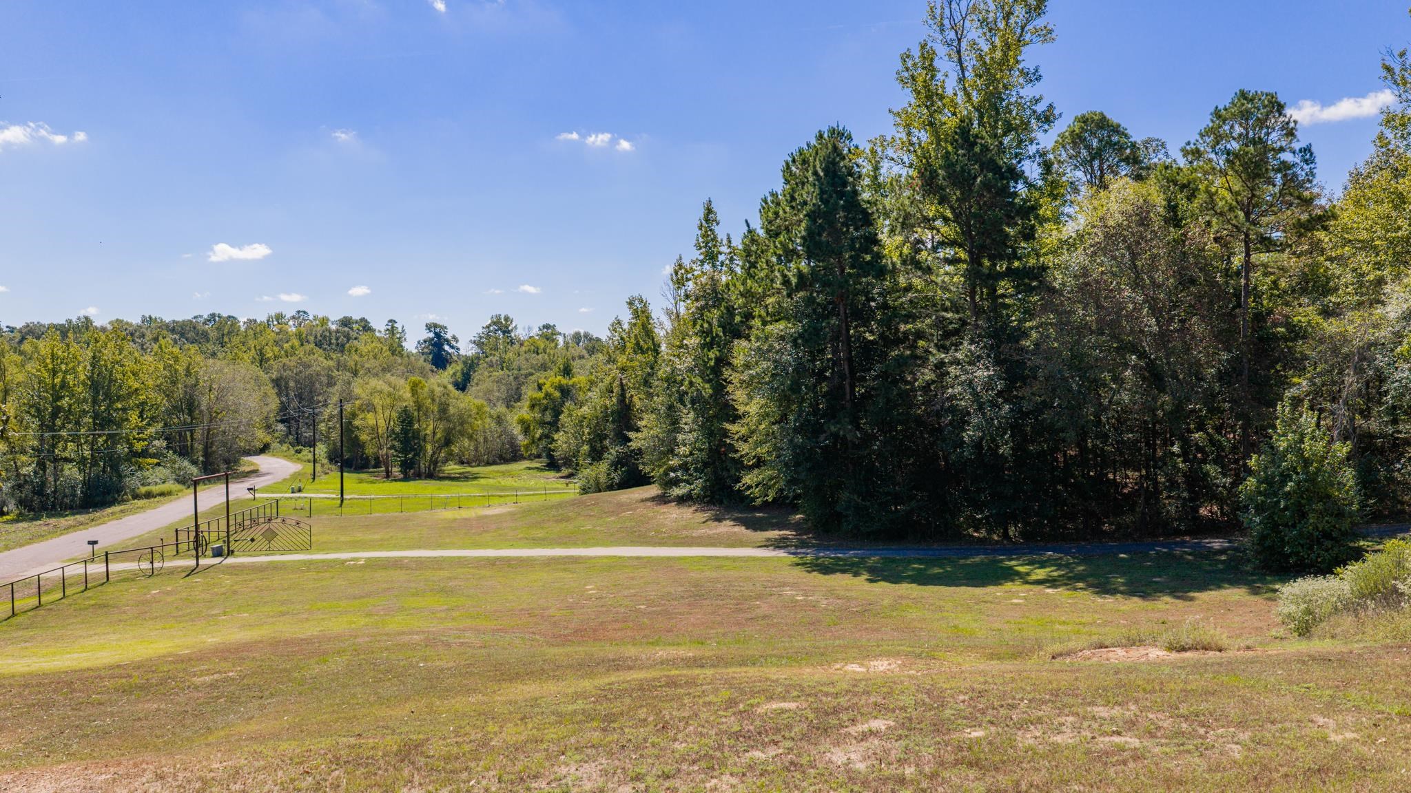 Open grassy property bordered by trees, with a curving driveway and metal gate.