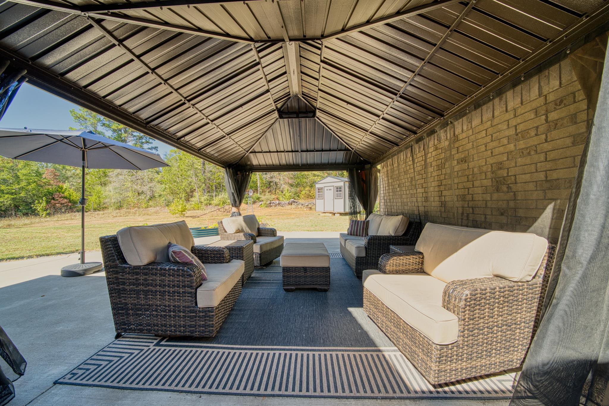 Covered patio with wicker seating, a striped rug, and a metal roof beside a brick wall.