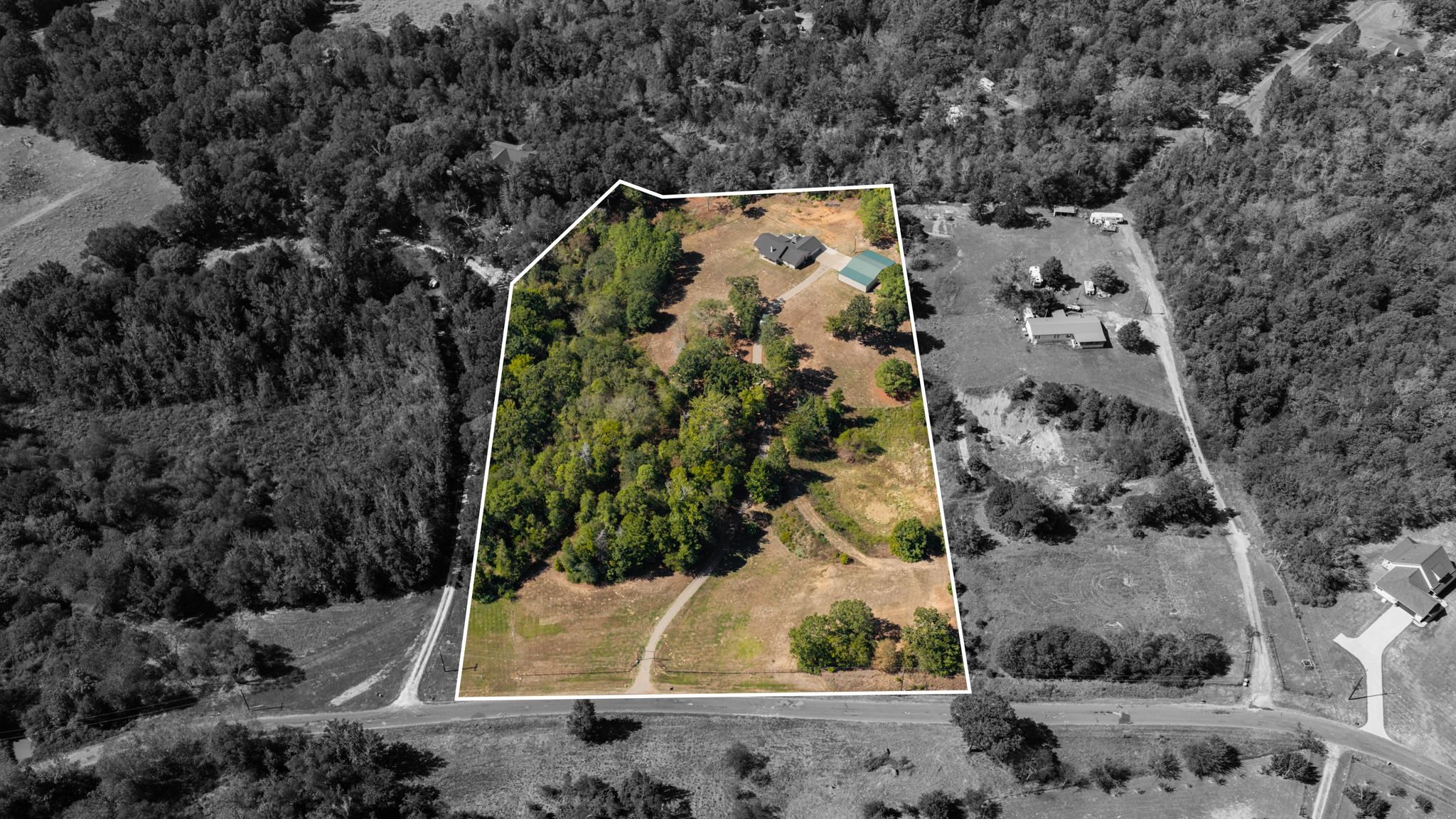 Aerial view of wooded acreage outlined in white, with a house, detached outbuilding, and road access.