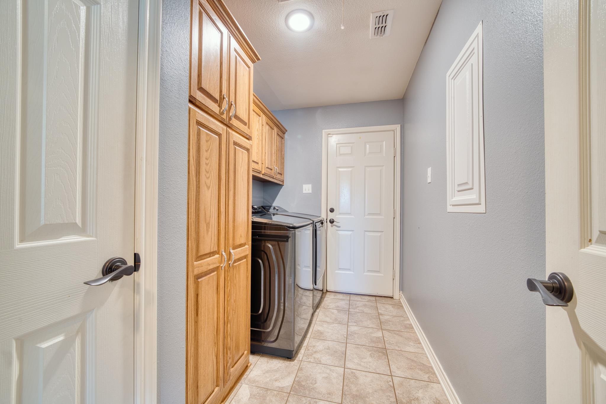 Laundry room with wood cabinetry, washer and dryer, and tiled floor.