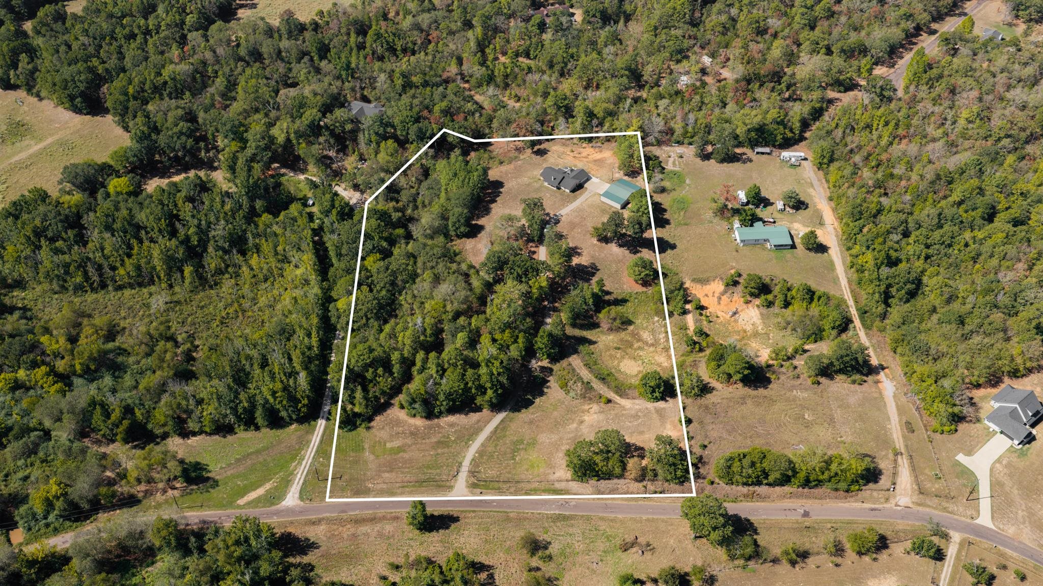 Aerial view of a wooded property with a house and outbuilding, outlined in white beside a road.