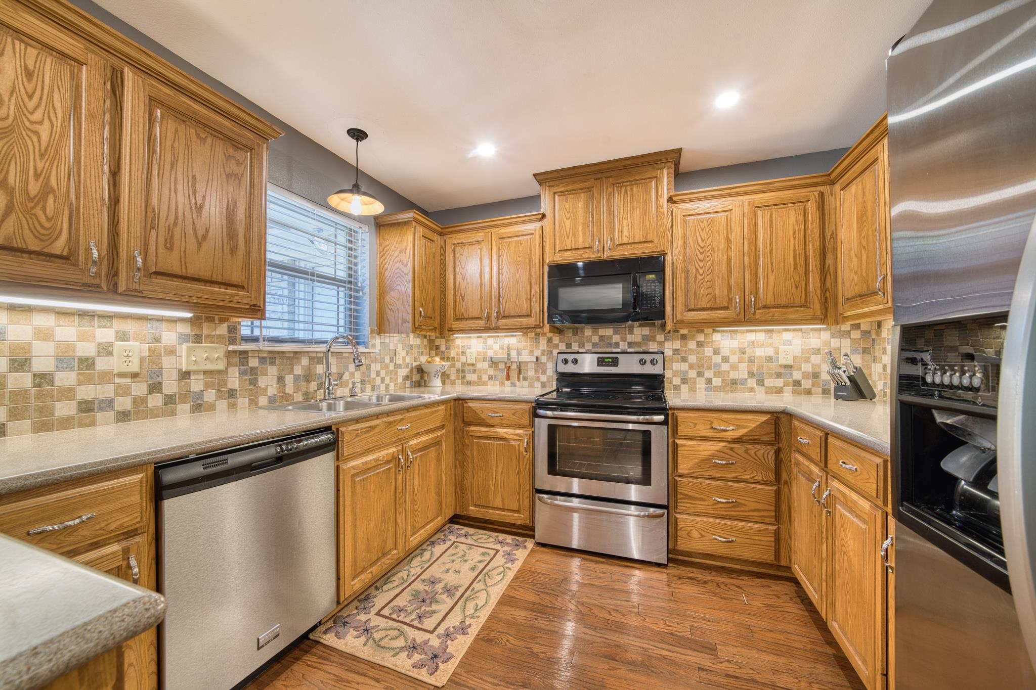 Kitchen with oak cabinets, tiled backsplash, stainless steel appliances, and a patterned runner rug.