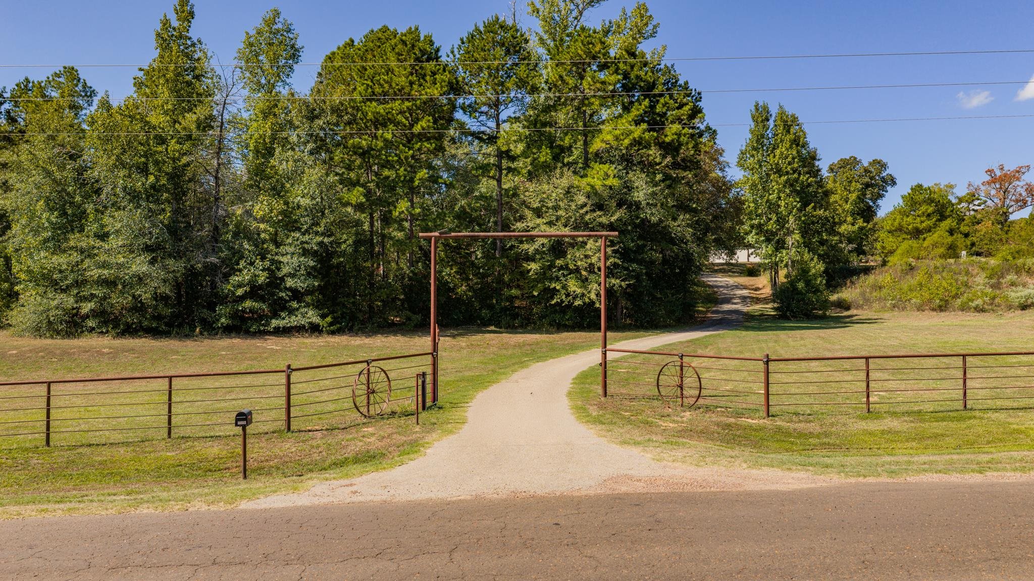 Gravel driveway through a rust-colored metal gate into a wooded rural property.