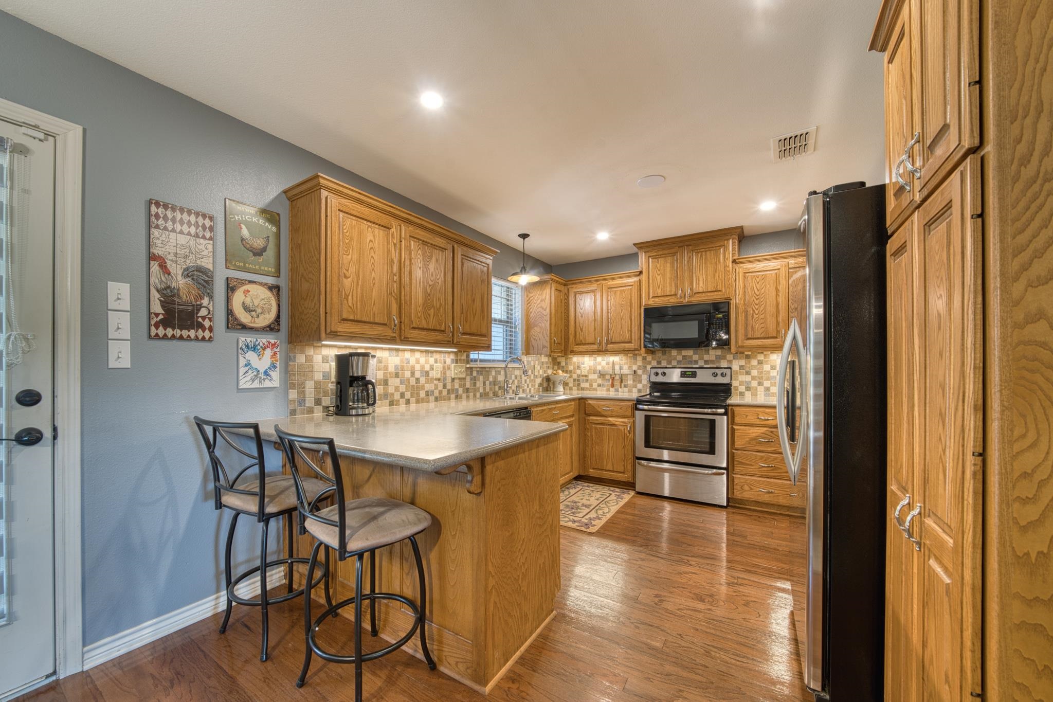 Kitchen with a wood island and bar stools, tiled backsplash, and stainless steel appliances.