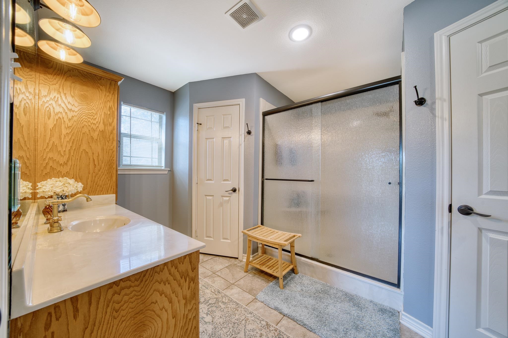 Bathroom with a glass-enclosed shower, wood-grain vanity, and tiled floor.
