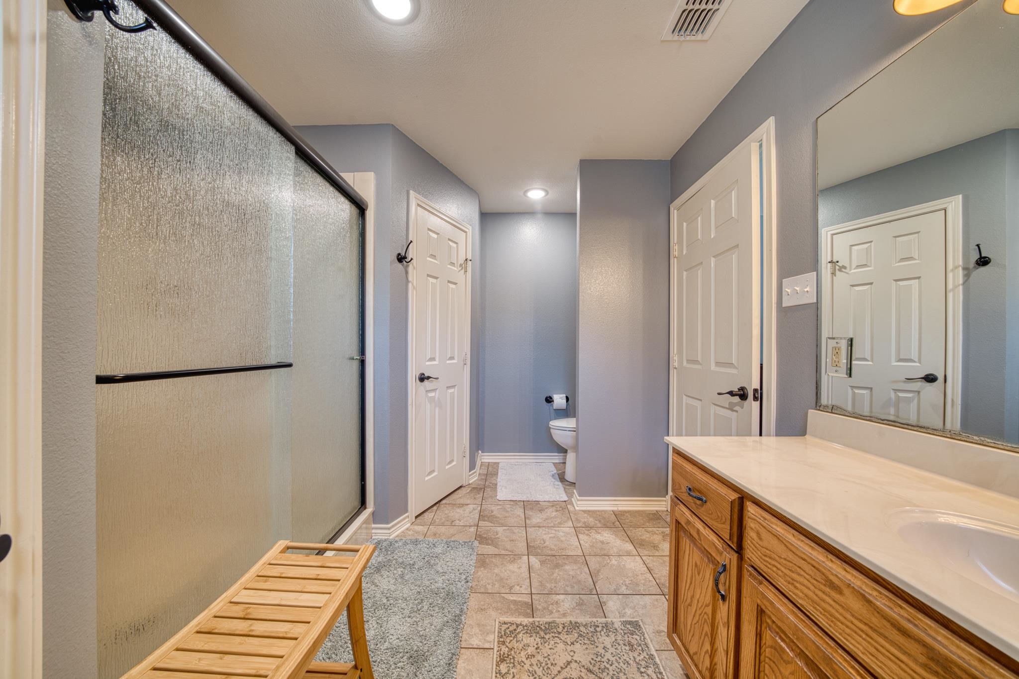 Bathroom with a glass shower, wood vanity, large mirror, and tiled floor.