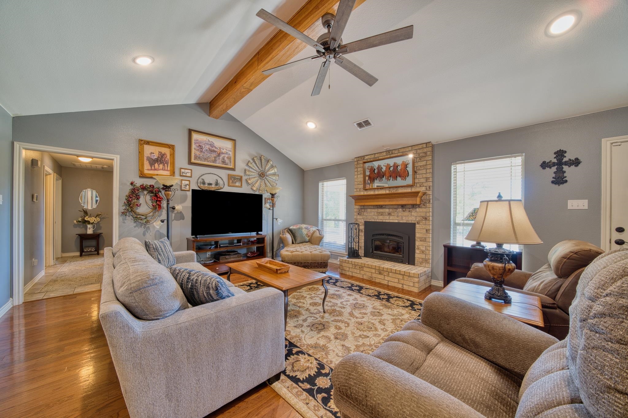 Furnished living room with vaulted ceiling, exposed wood beam, and brick fireplace.