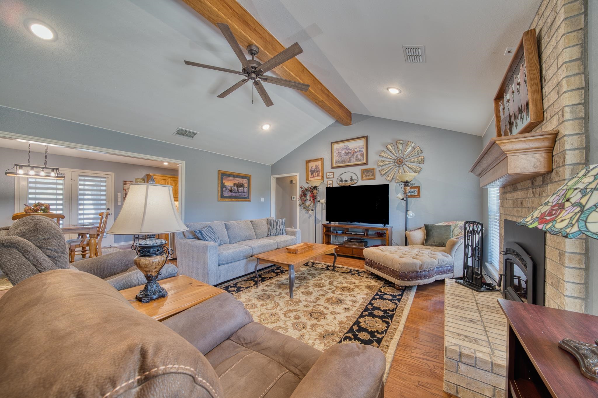 Living room with a vaulted wood-beam ceiling, brick fireplace, and adjoining dining area.
