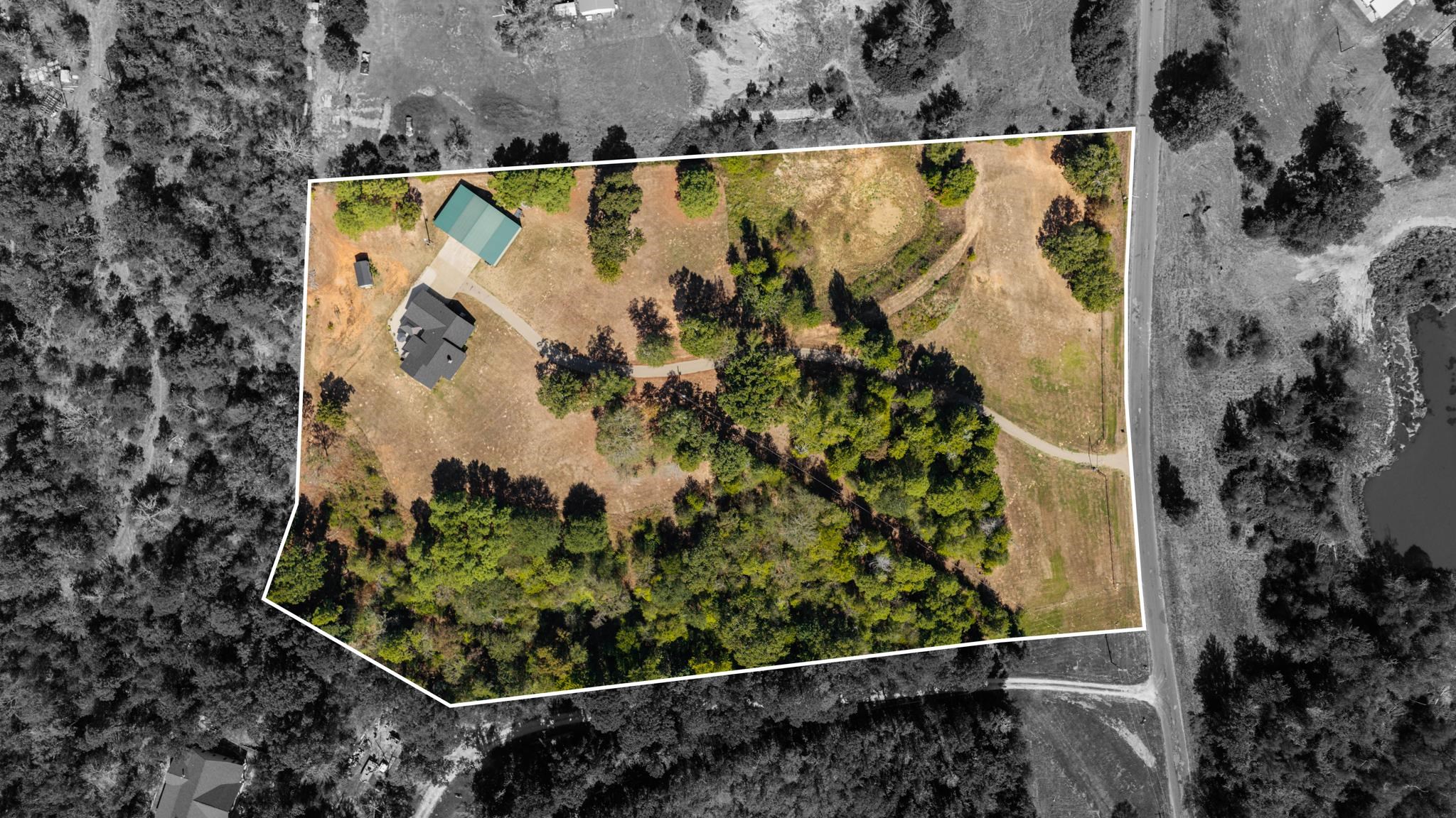 Aerial view of a home and outbuilding on a tree-lined lot, outlined in white.