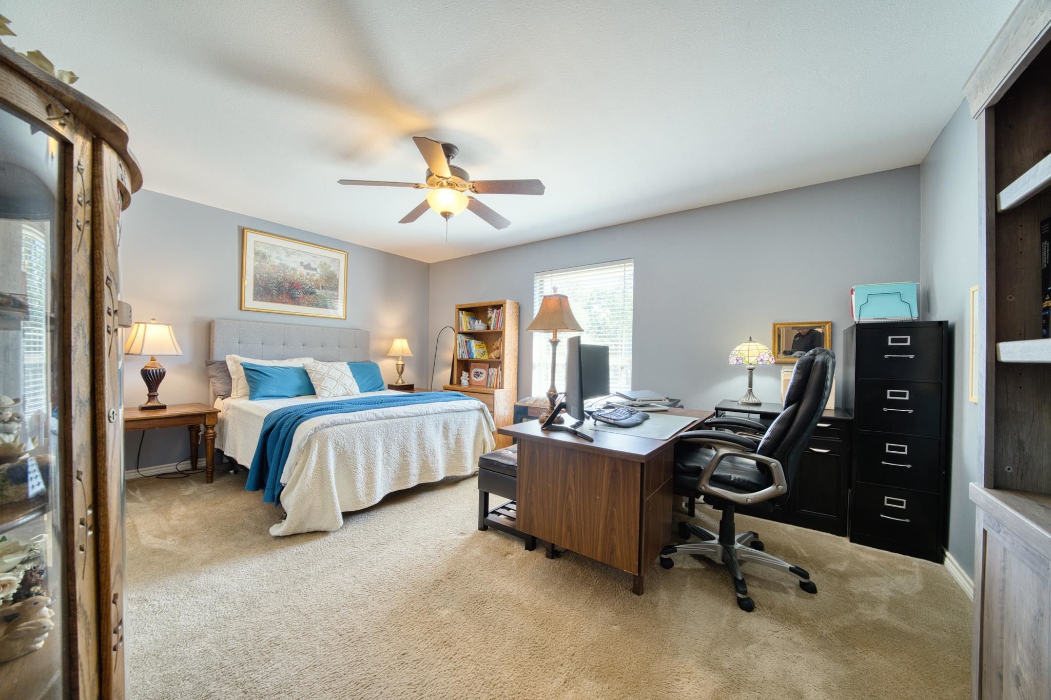 Bedroom and home office with a blue-accented bed, wooden desk, and computer chairs.