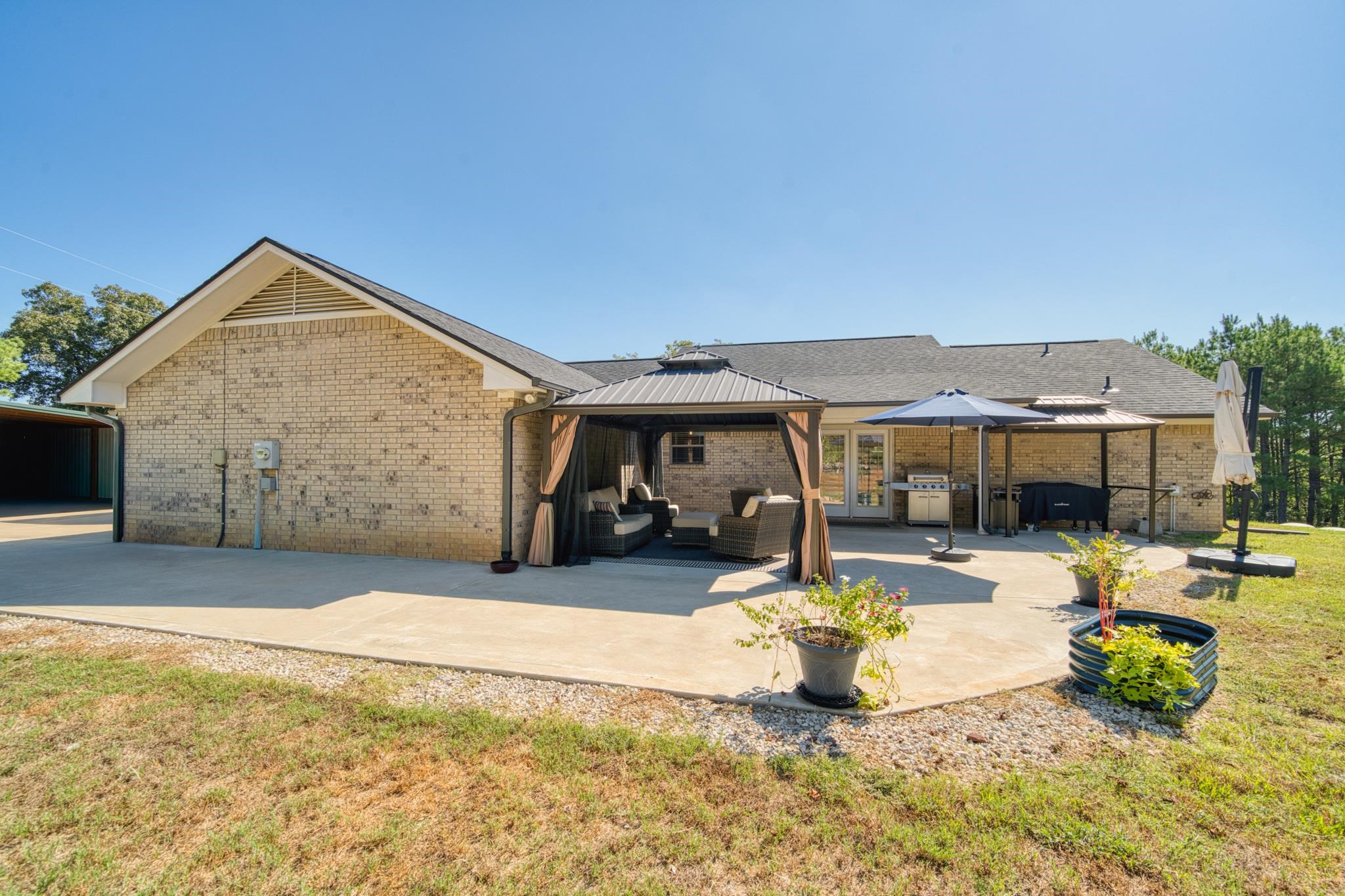 Tan brick home with a spacious patio, curtained gazebo, umbrella, and covered outdoor cooking area.