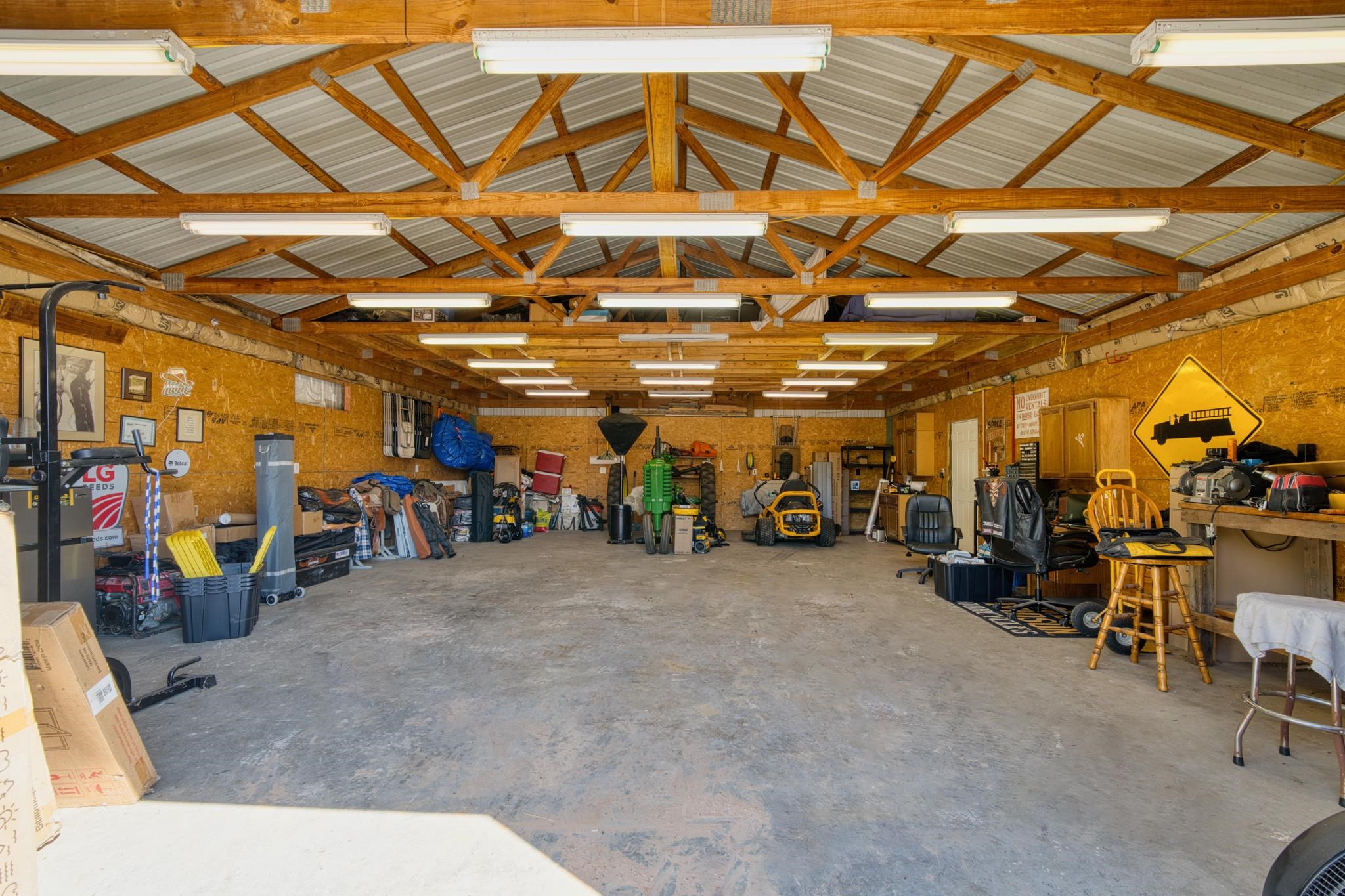 Large workshop garage with exposed timber trusses, fluorescent lights, and equipment lining the walls.