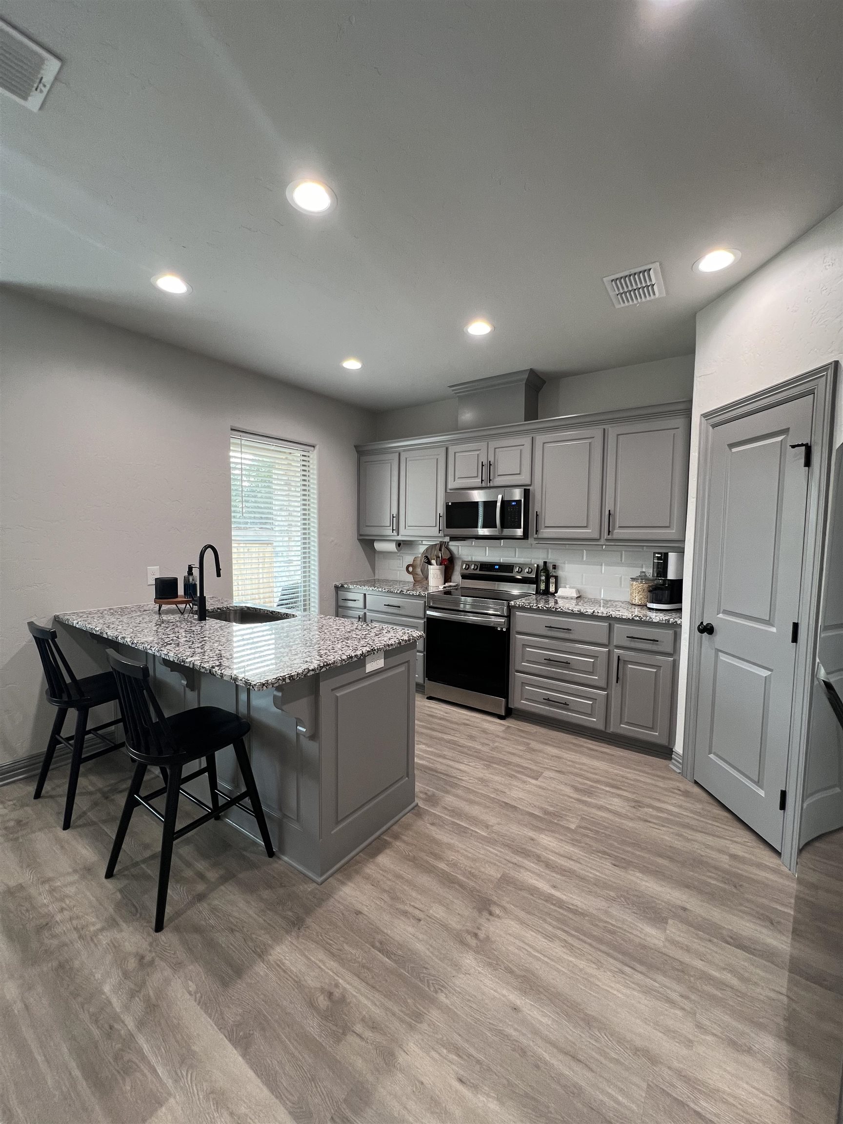 Kitchen with gray cabinets, stainless steel appliances, and a granite island with bar stools.