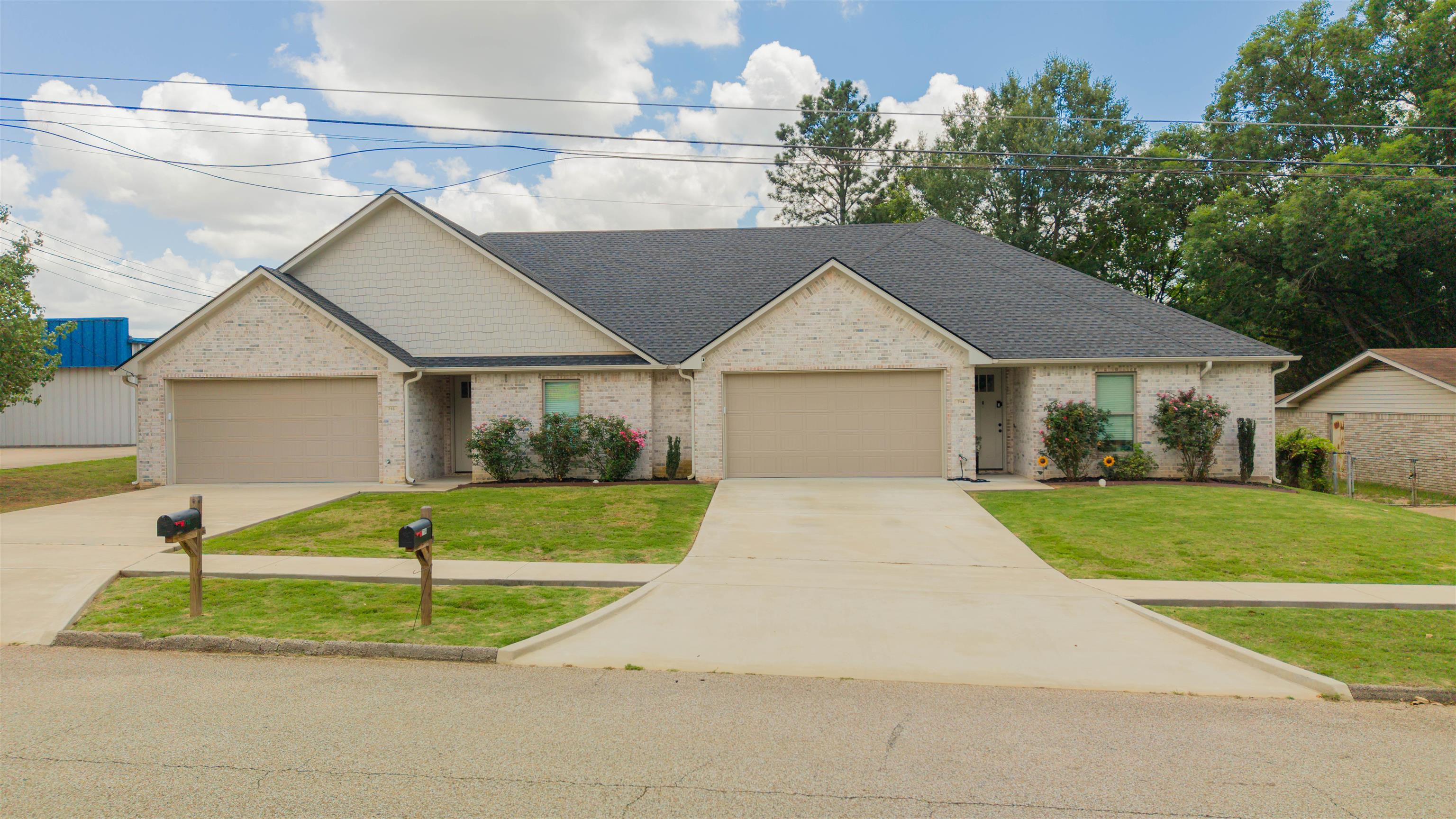 Brick duplex with two garage doors, separate entrances, and broad concrete driveways.