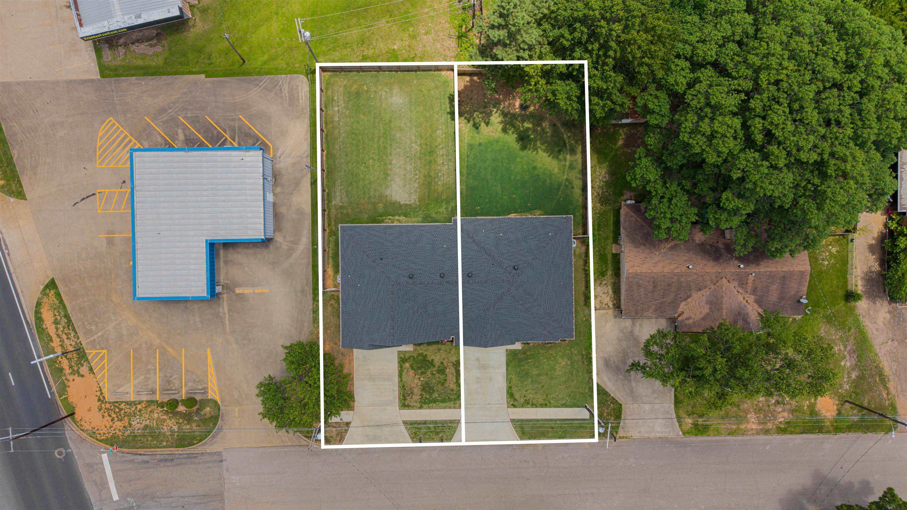 Aerial view of a house and lot outlined in white, with driveway and neighboring properties.