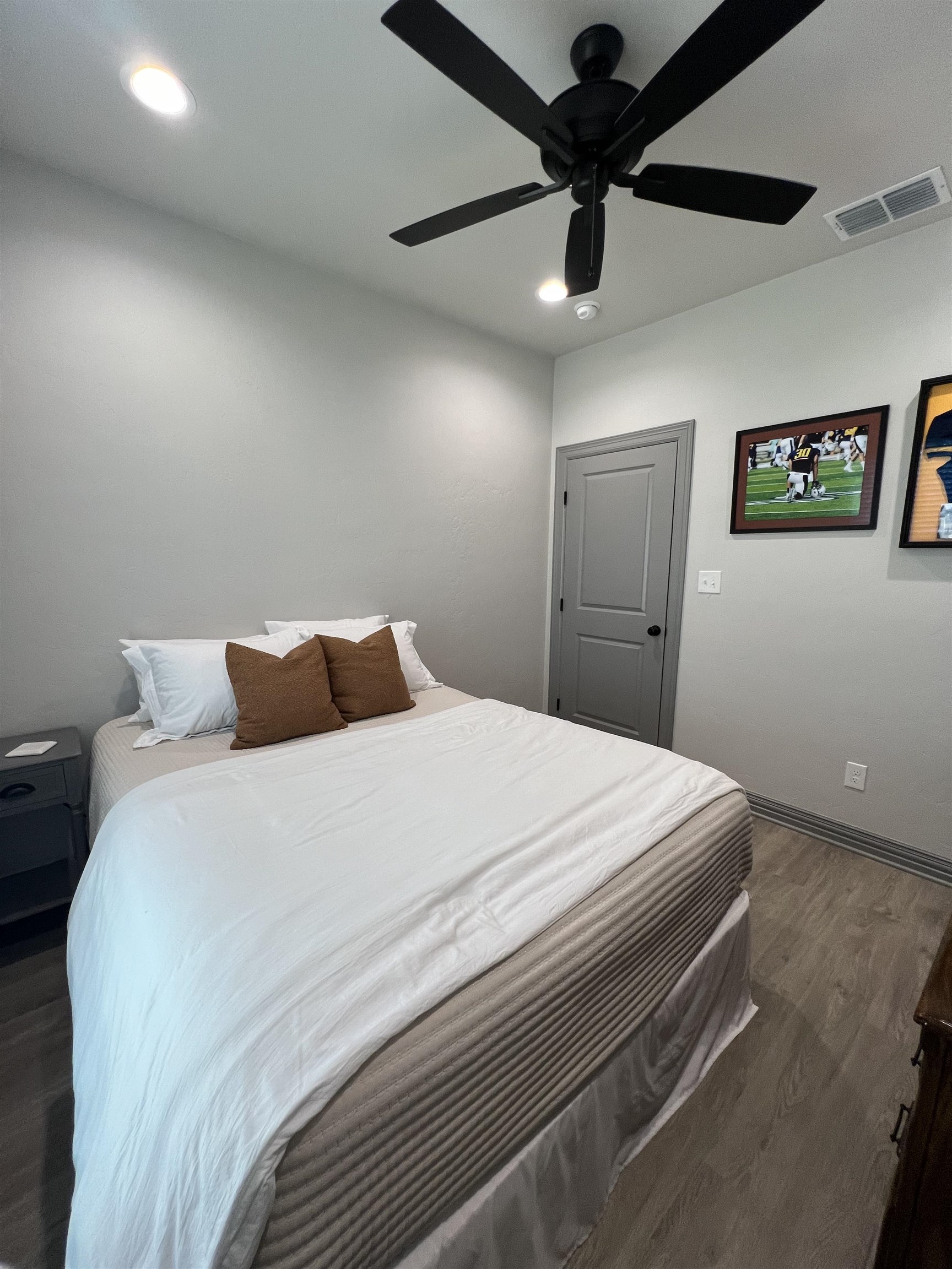 Furnished bedroom with a white bed, brown pillows, and a black ceiling fan.