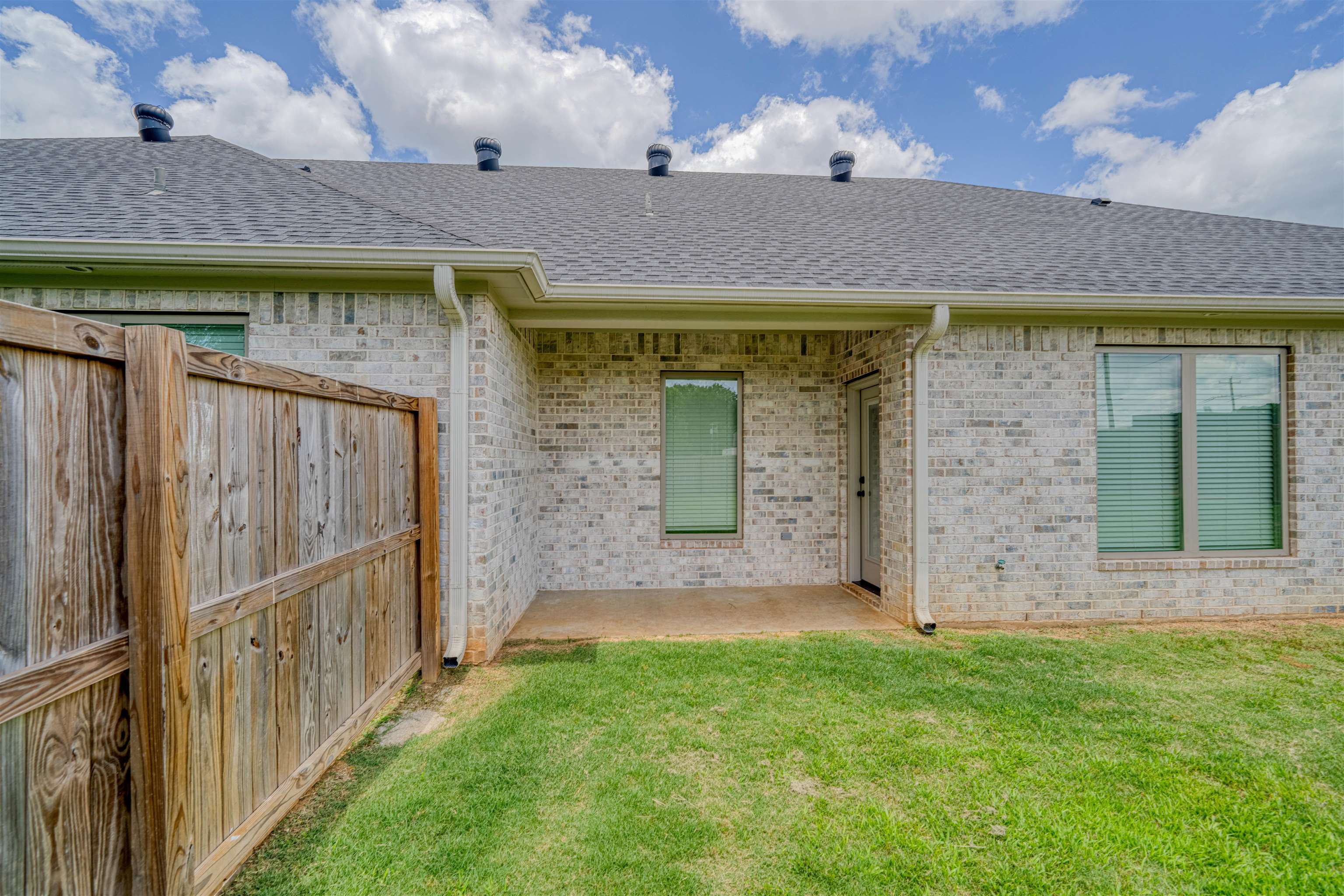 Rear of a brick house with a covered patio, lawn, and wooden privacy fence.