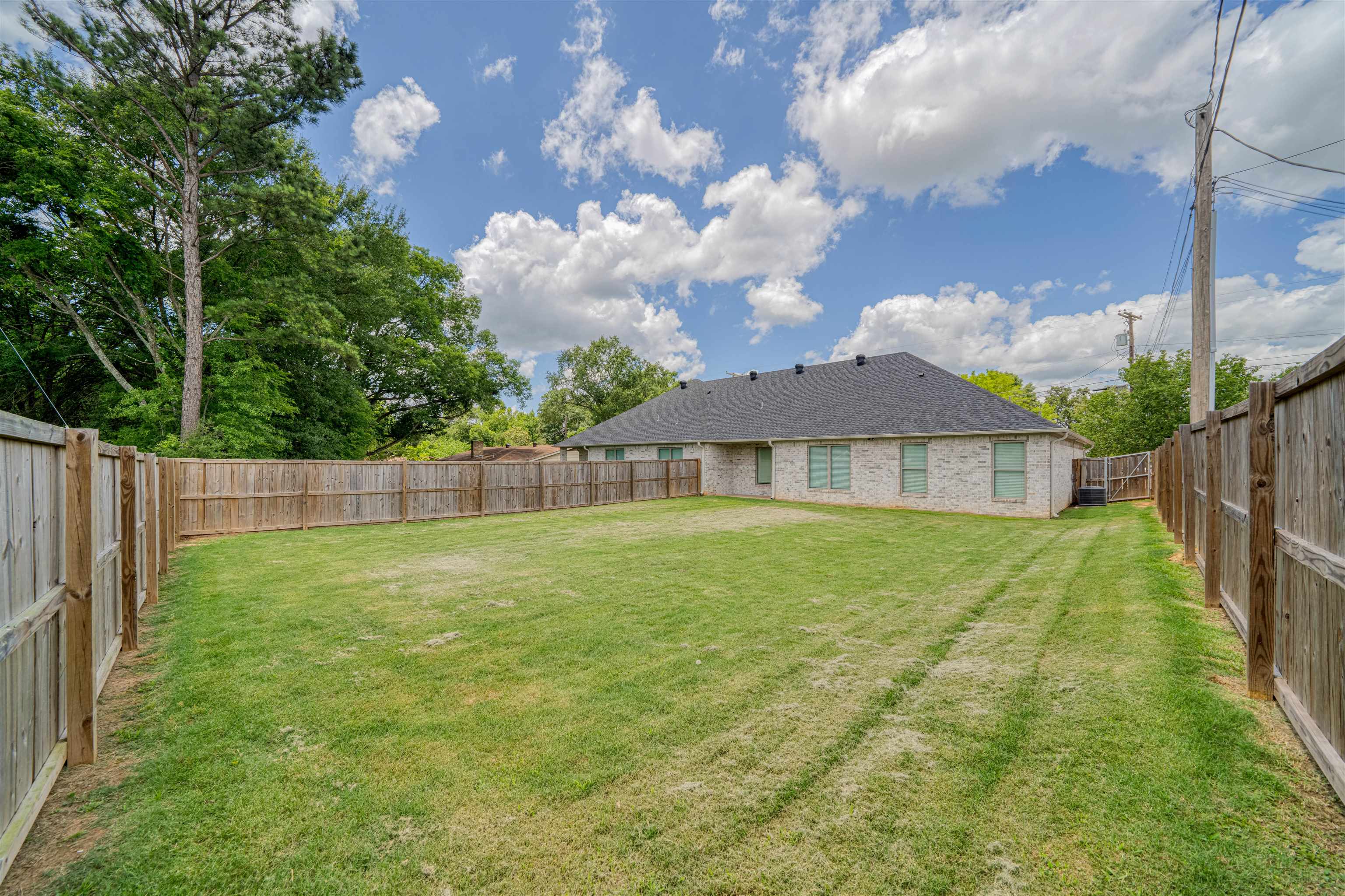 Brick house behind a broad fenced backyard with a grassy lawn and mature trees.