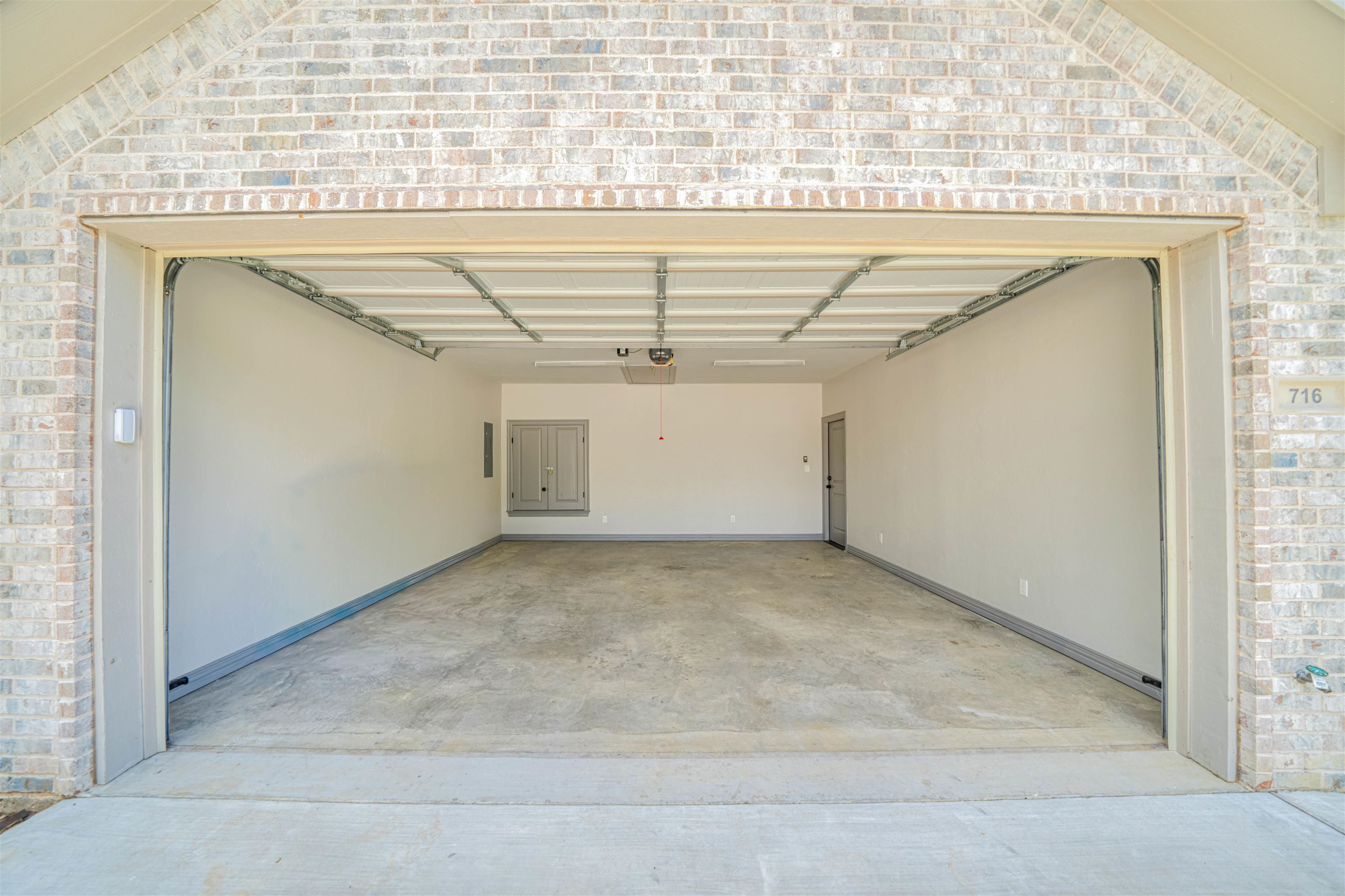 Empty two-car garage with its overhead door raised, showing a concrete floor and light brick exterior.