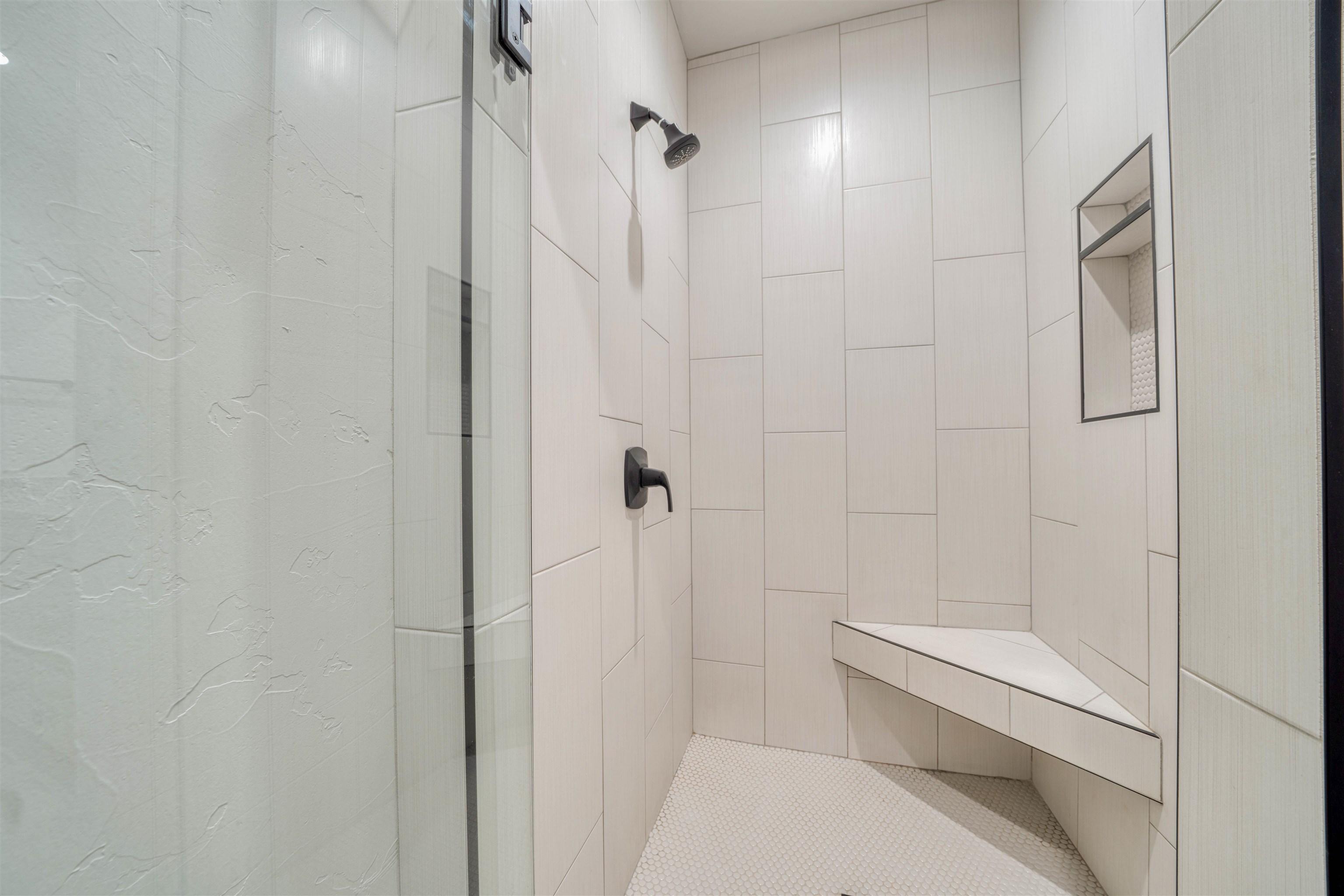 Walk-in shower with a tiled bench, recessed niche, and black fixtures.