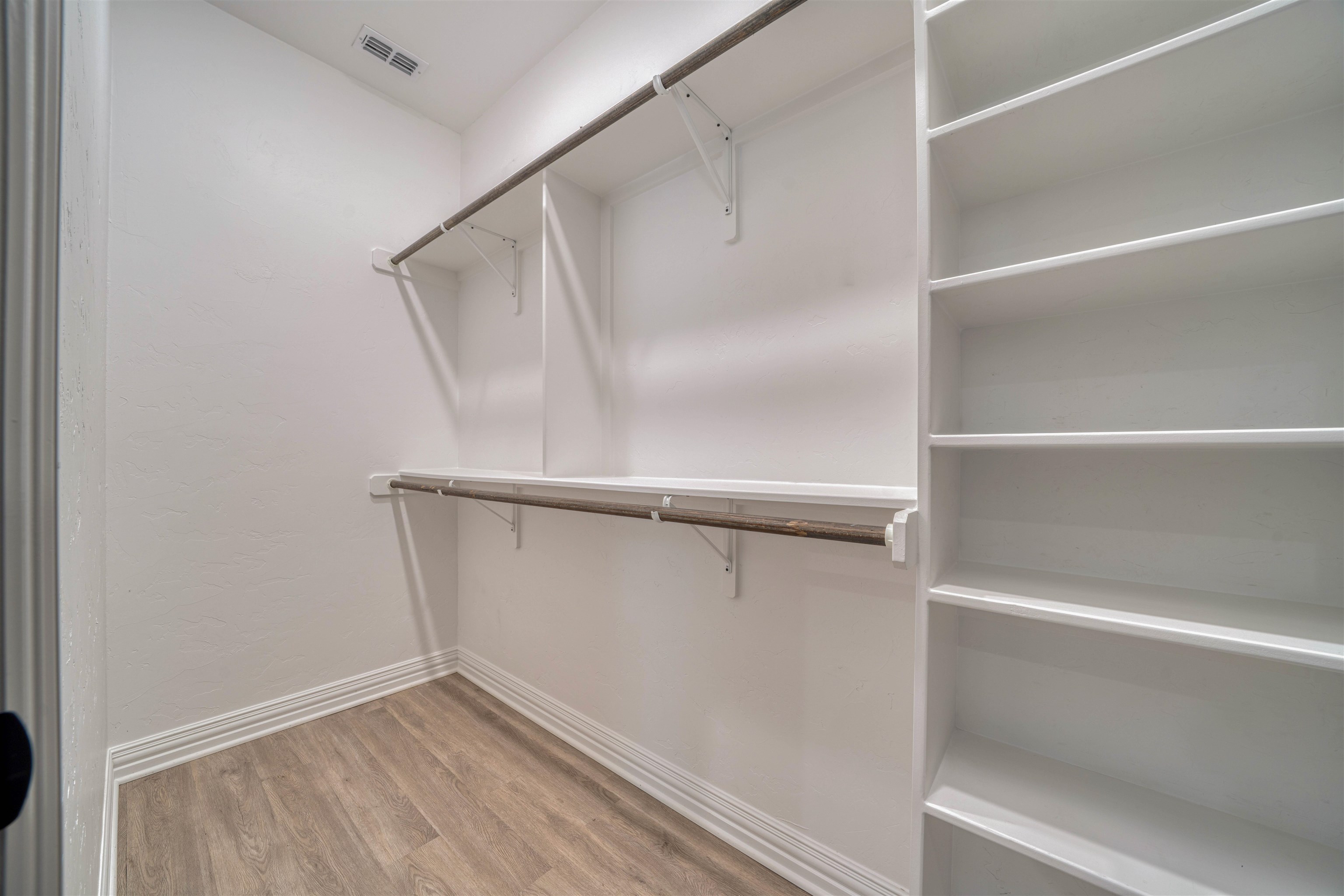 Walk-in closet with white shelving, two hanging rods, and wood-look flooring.
