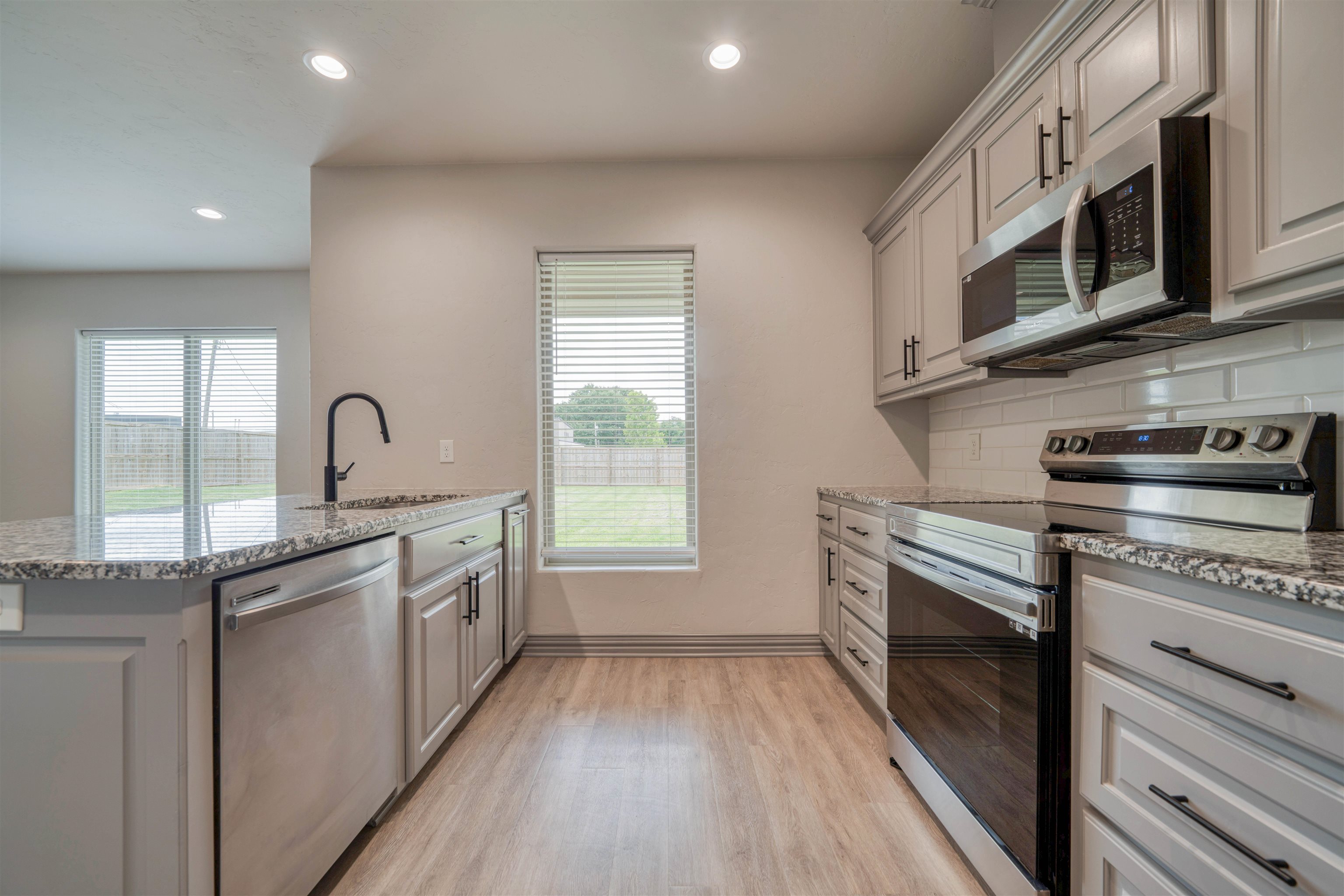 Kitchen with white cabinets, granite counters, stainless appliances, and windows overlooking a fenced yard.