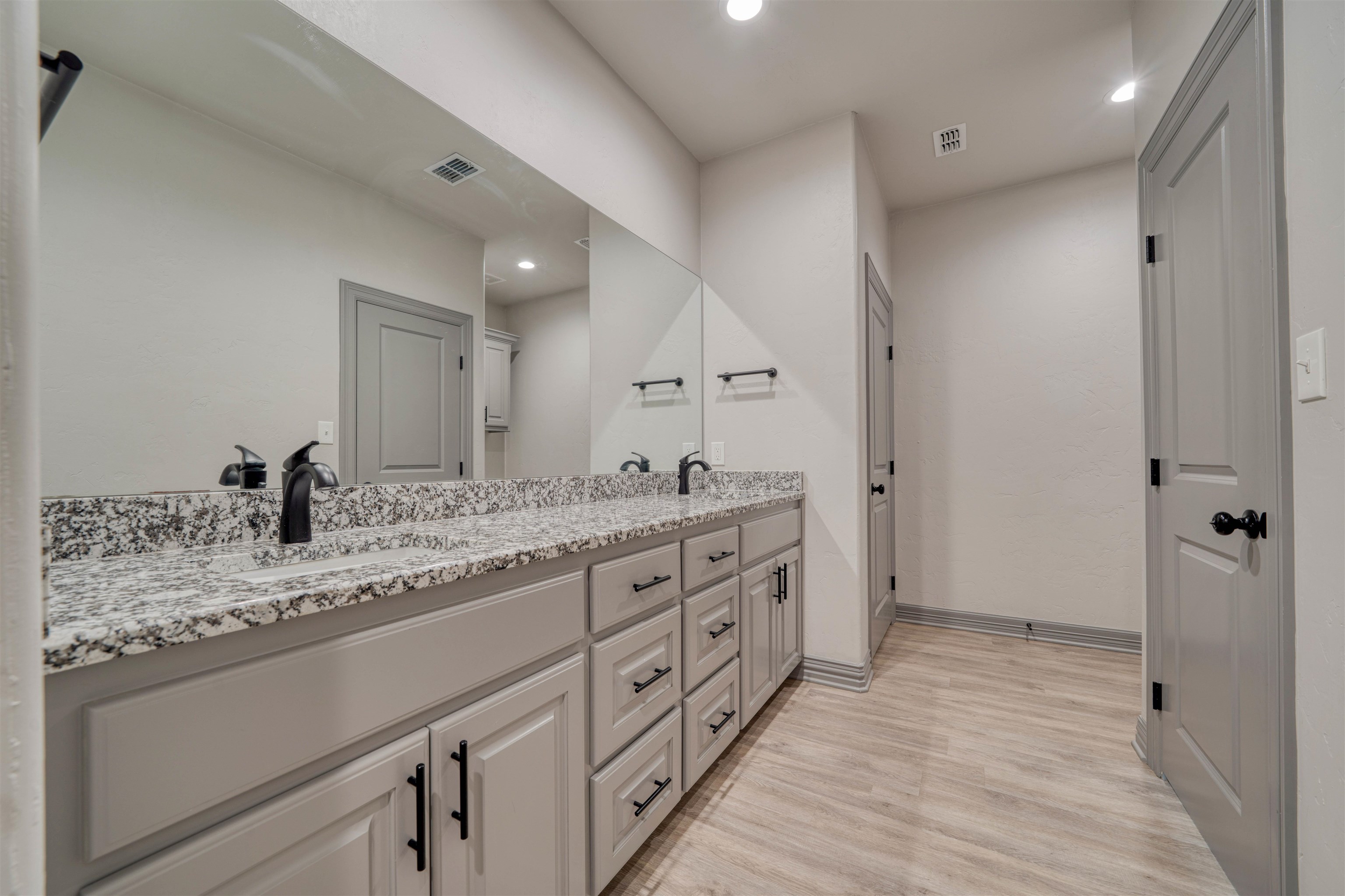 Bathroom vanity with a speckled granite counter, large mirror, gray cabinets, and black faucets.