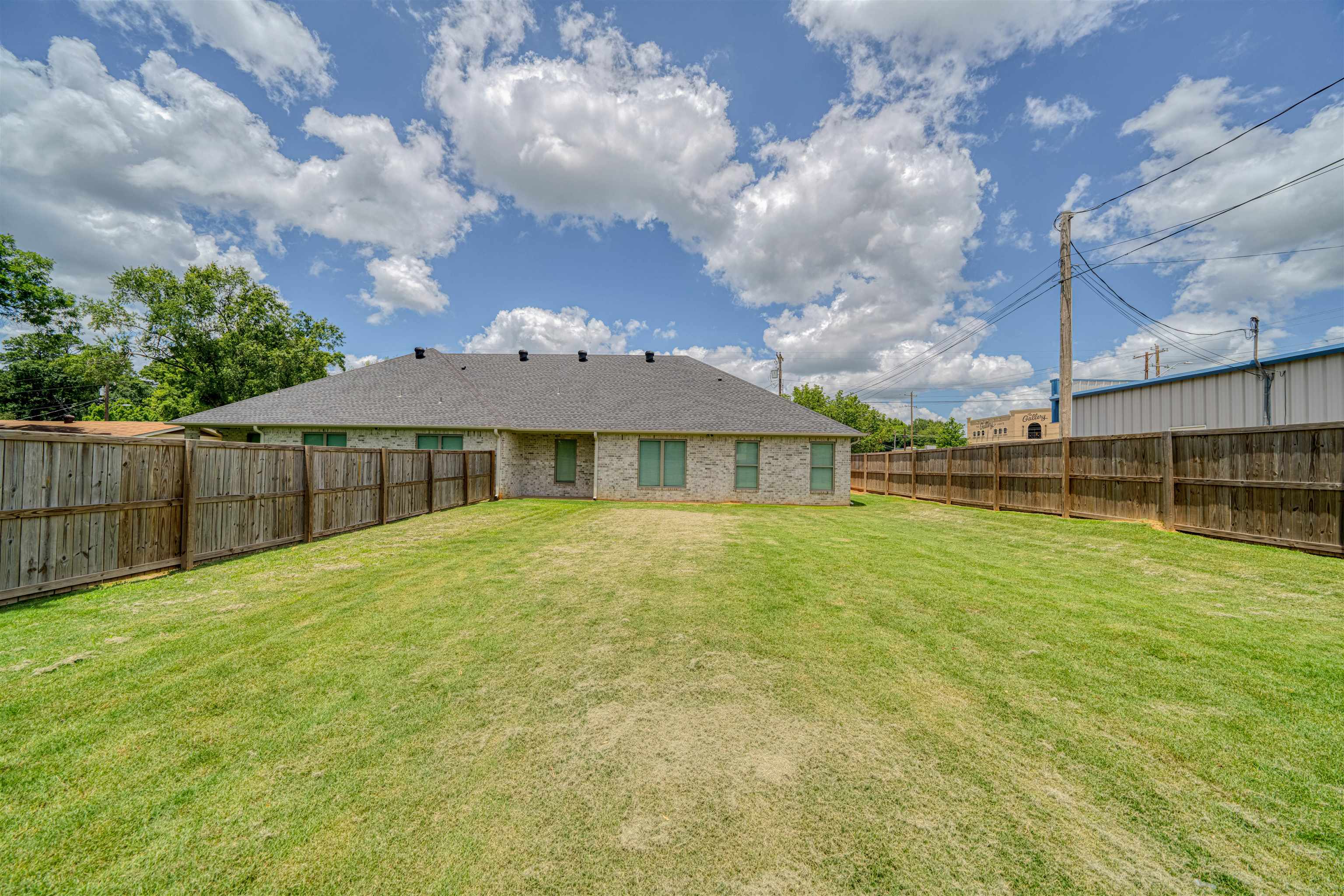 Brick home behind a broad grassy backyard enclosed by wooden fencing.