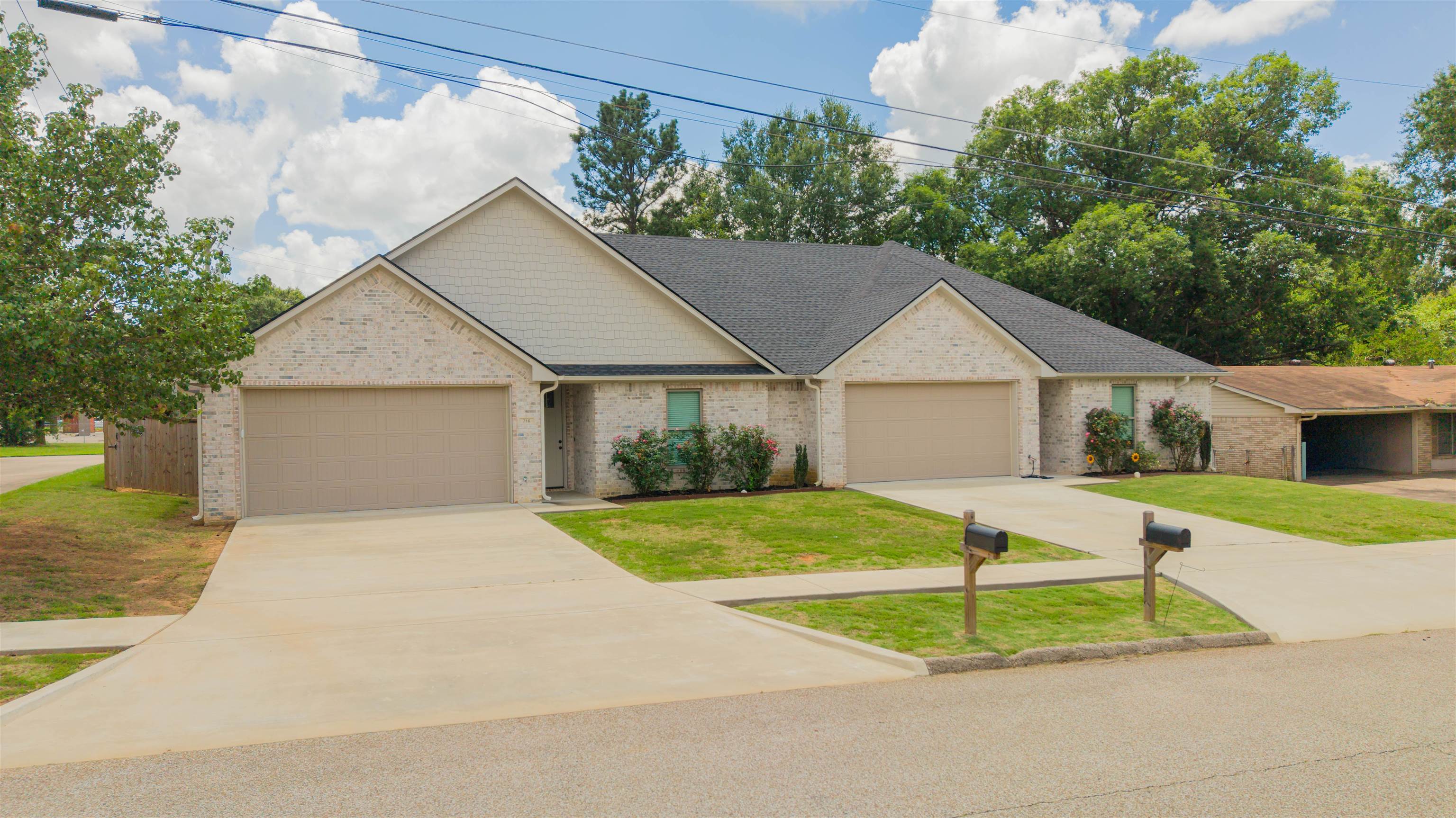 Light brick home with two garage doors, landscaped front beds, and wide concrete driveways.