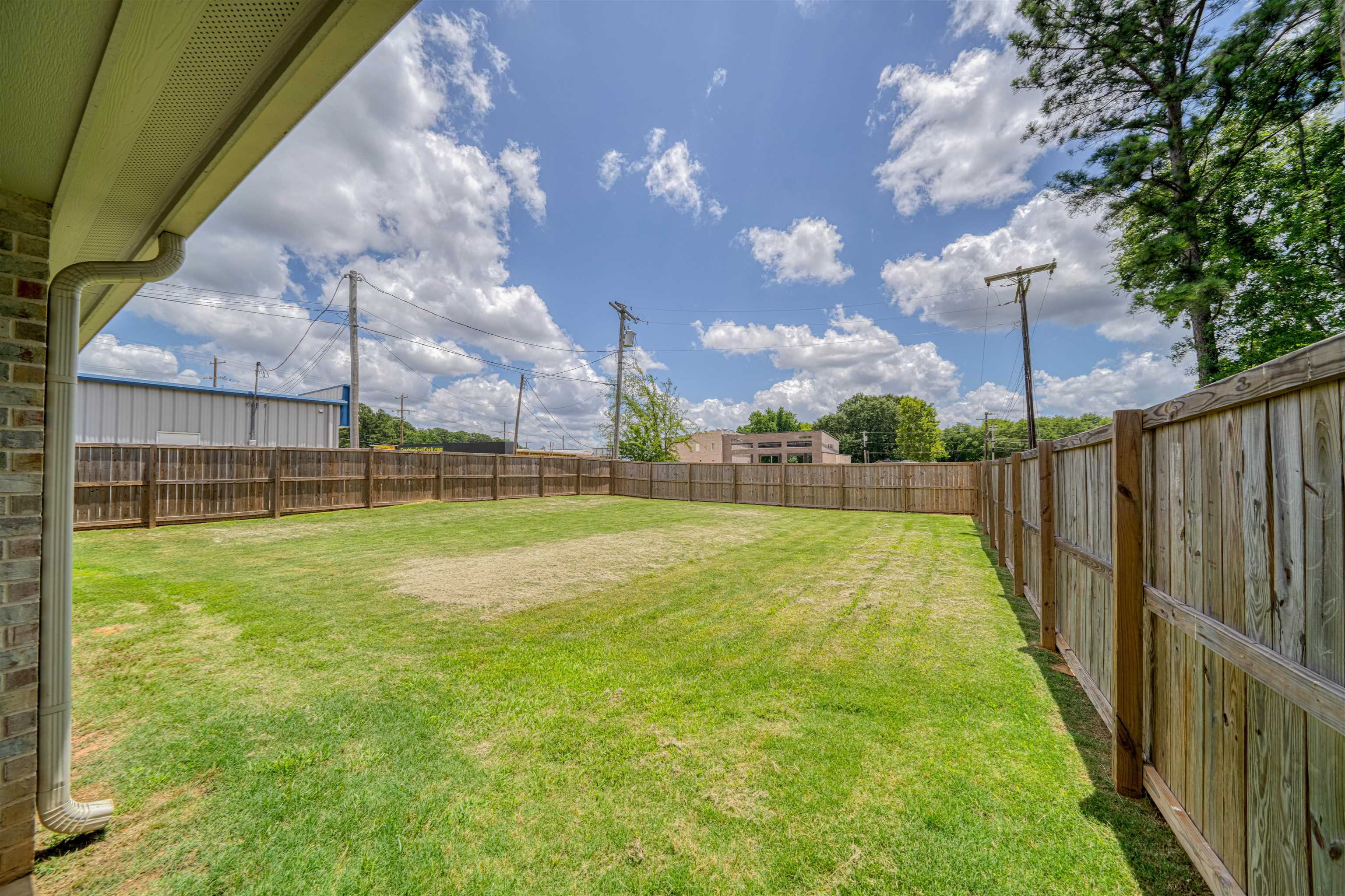 Fenced grassy backyard with a wide lawn and neighboring buildings beyond the fence.